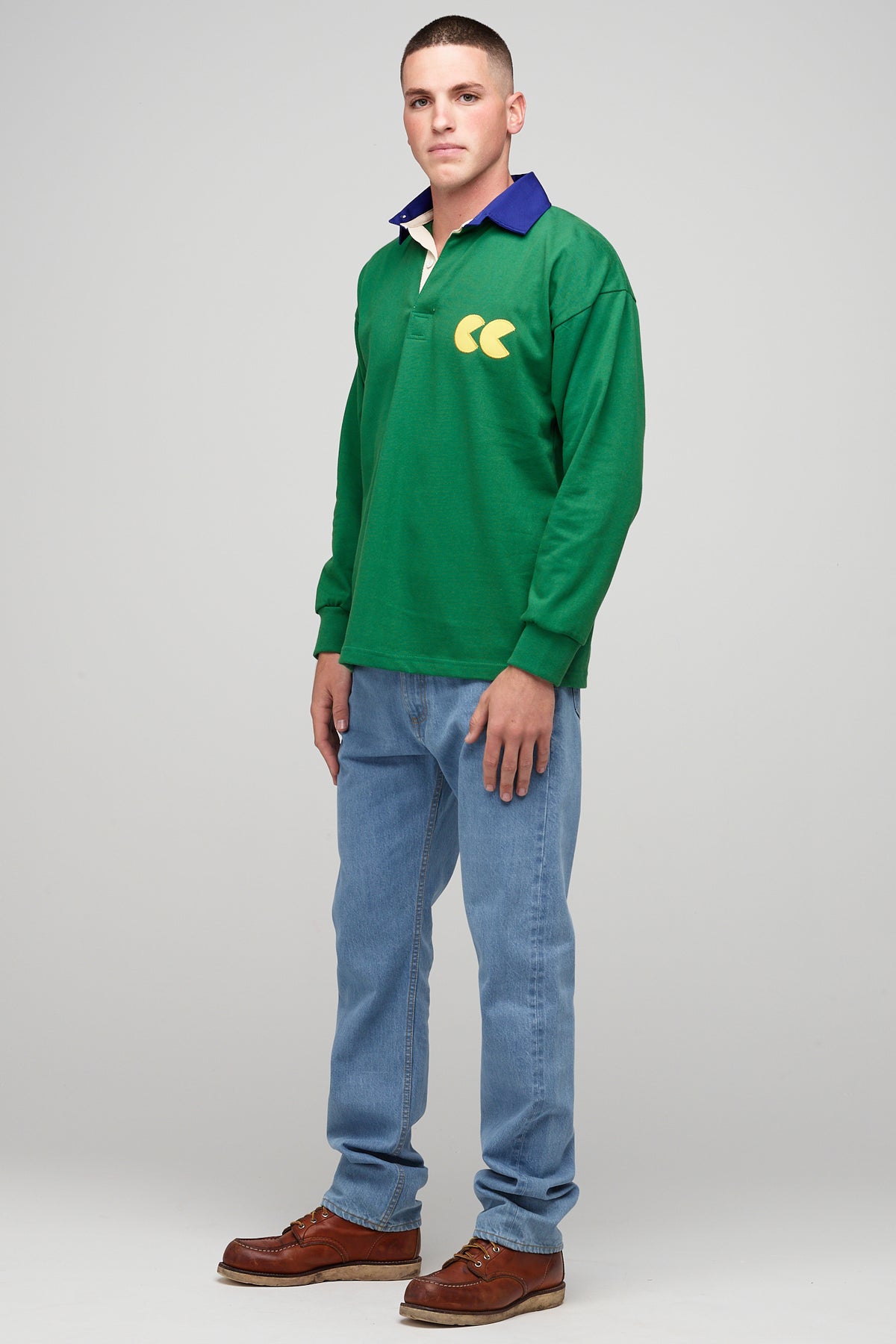 White, brunette male, wearing green rugby shirt with contrast blue collar, yellow CC logo badge 