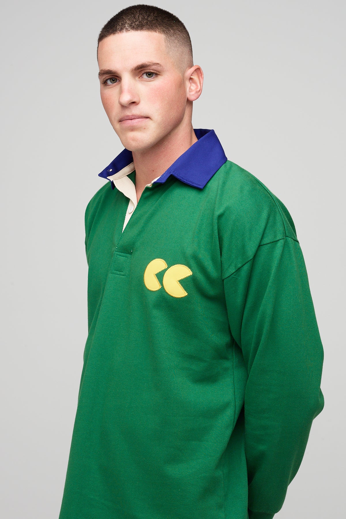 White, brunette male, wearing green rugby shirt with contrast blue collar, yellow CC logo badge 