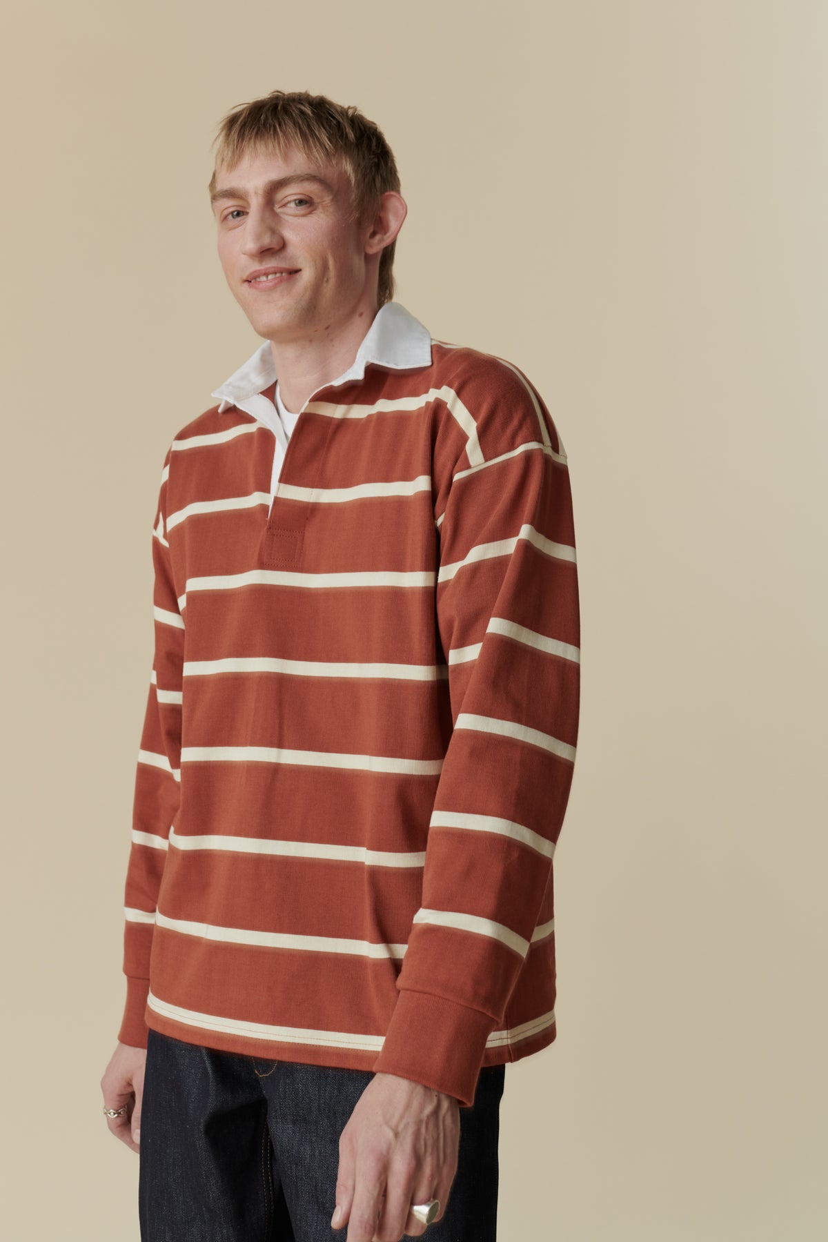 Thigh up shot of smiley, white male wearing rugby shirt in cinnamon and ecru stripe