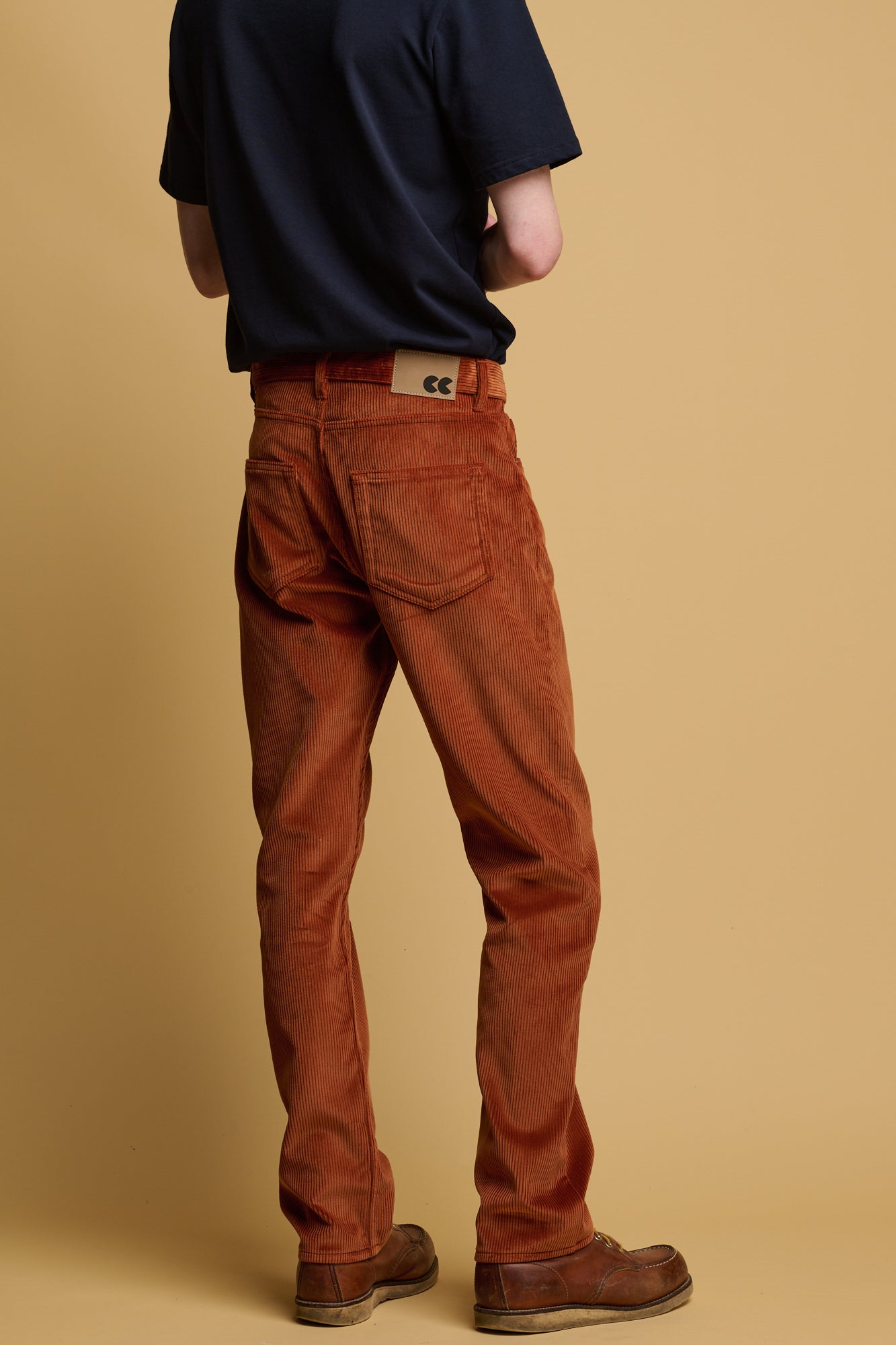 The front of male chest down wearing community clothing cord trousers in cinnamon  with CC logo silver button