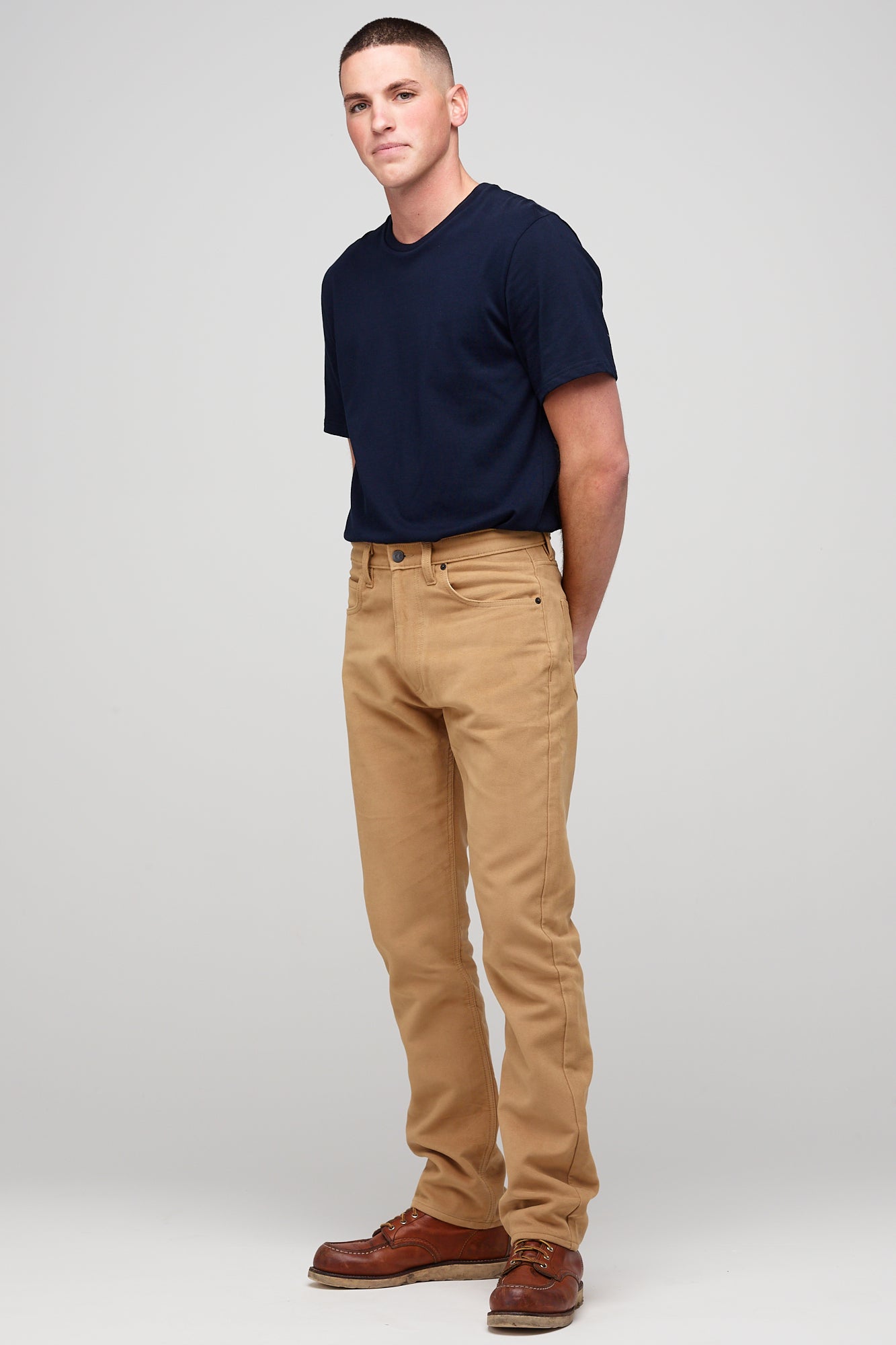 Male brunette wearing five pocket moleskin jeans in camel styled with black t-shirt tucked in paired with brown leather shoes