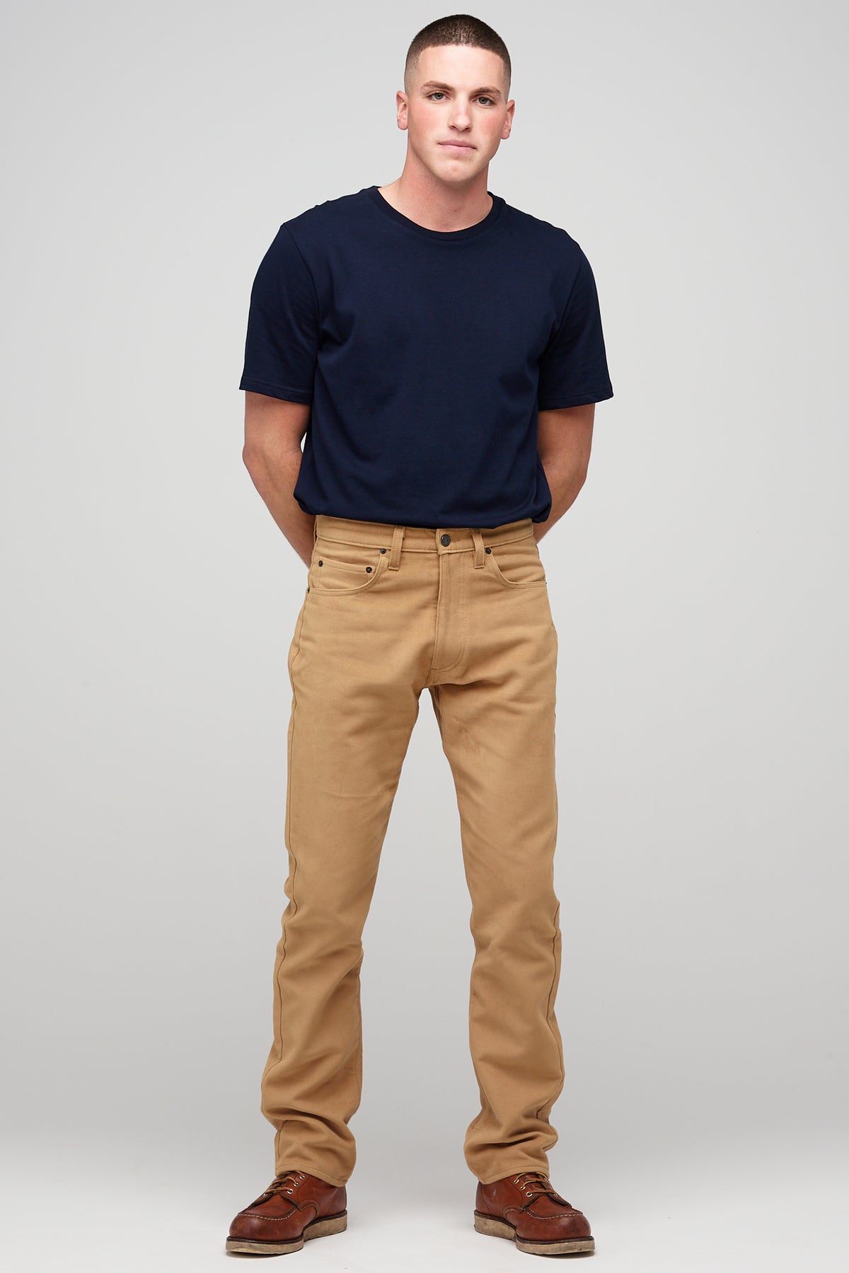 Male brunette wearing five pocket moleskin jeans in camel styled with black t-shirt tucked in paired with brown leather shoes