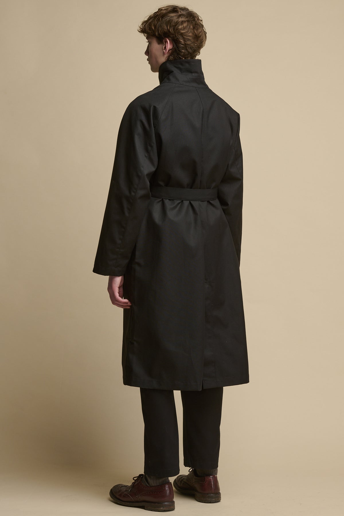 The back of male wearing Frank Raglan Belted Raincoat in black with collar up 