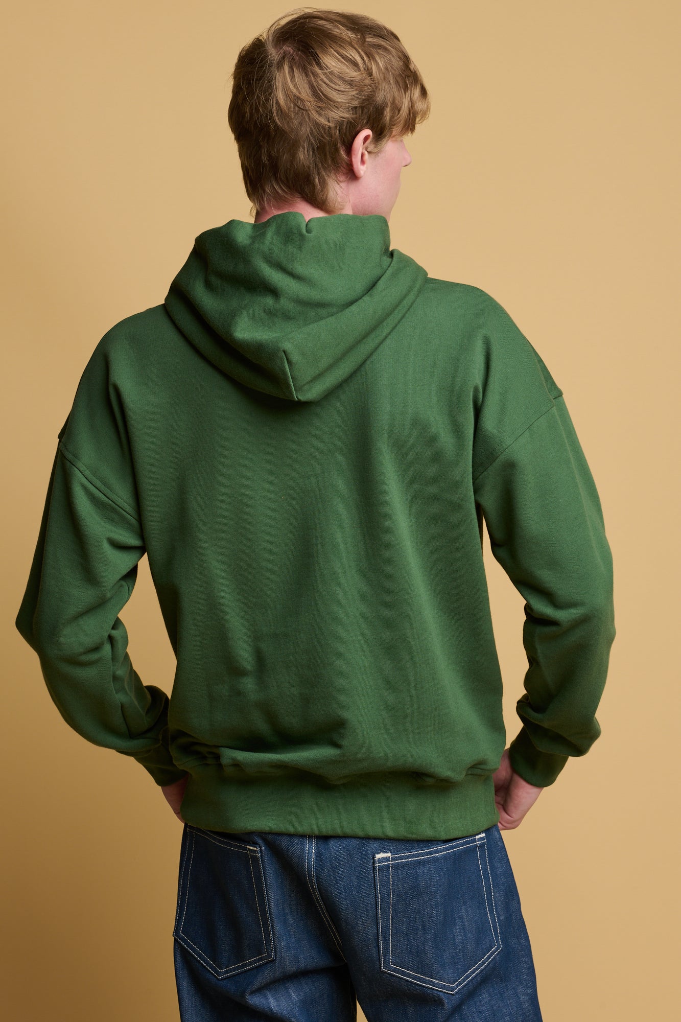 Thigh up image of male with his hands in the pocket of hooded sweatshirt in bottle green