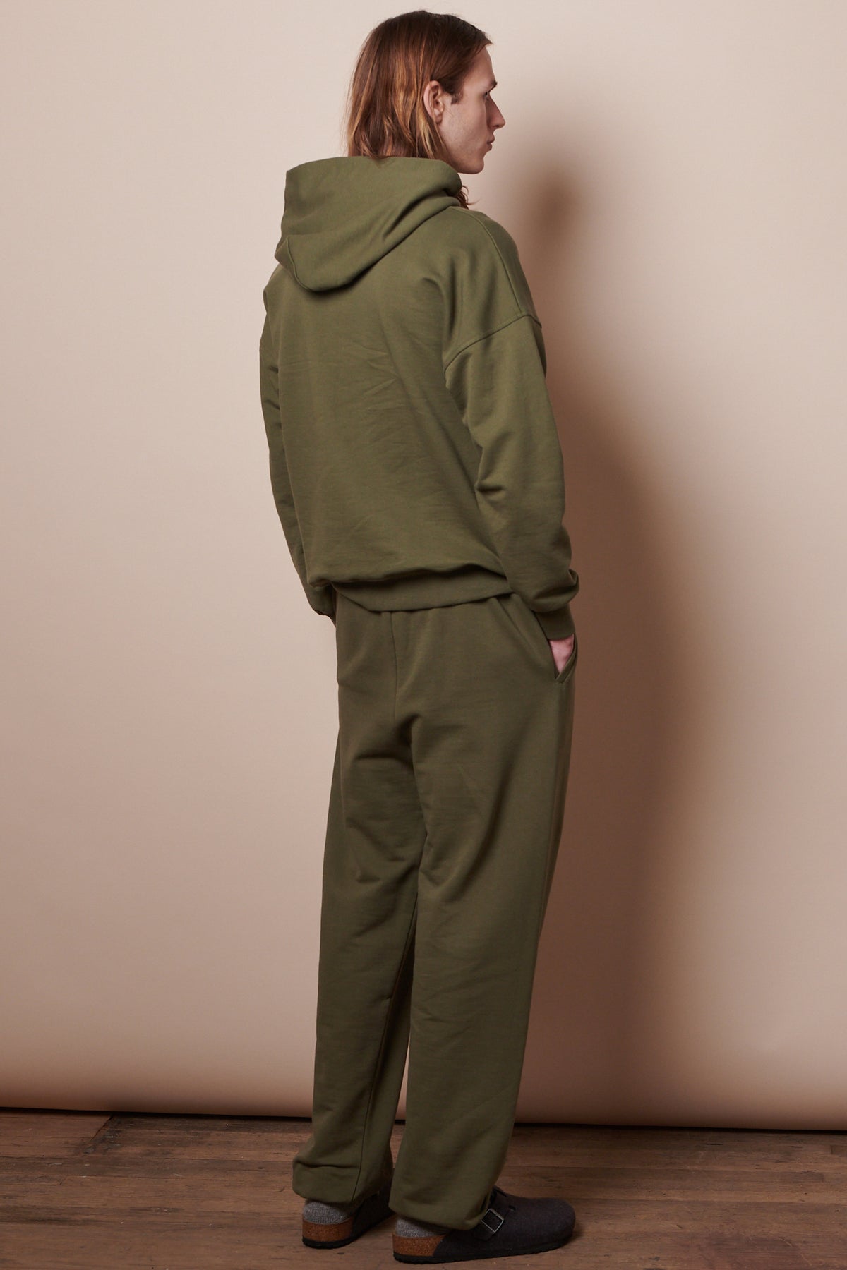 Back of male wearing hooded sweatshirt in olive paired with matching sweatpants