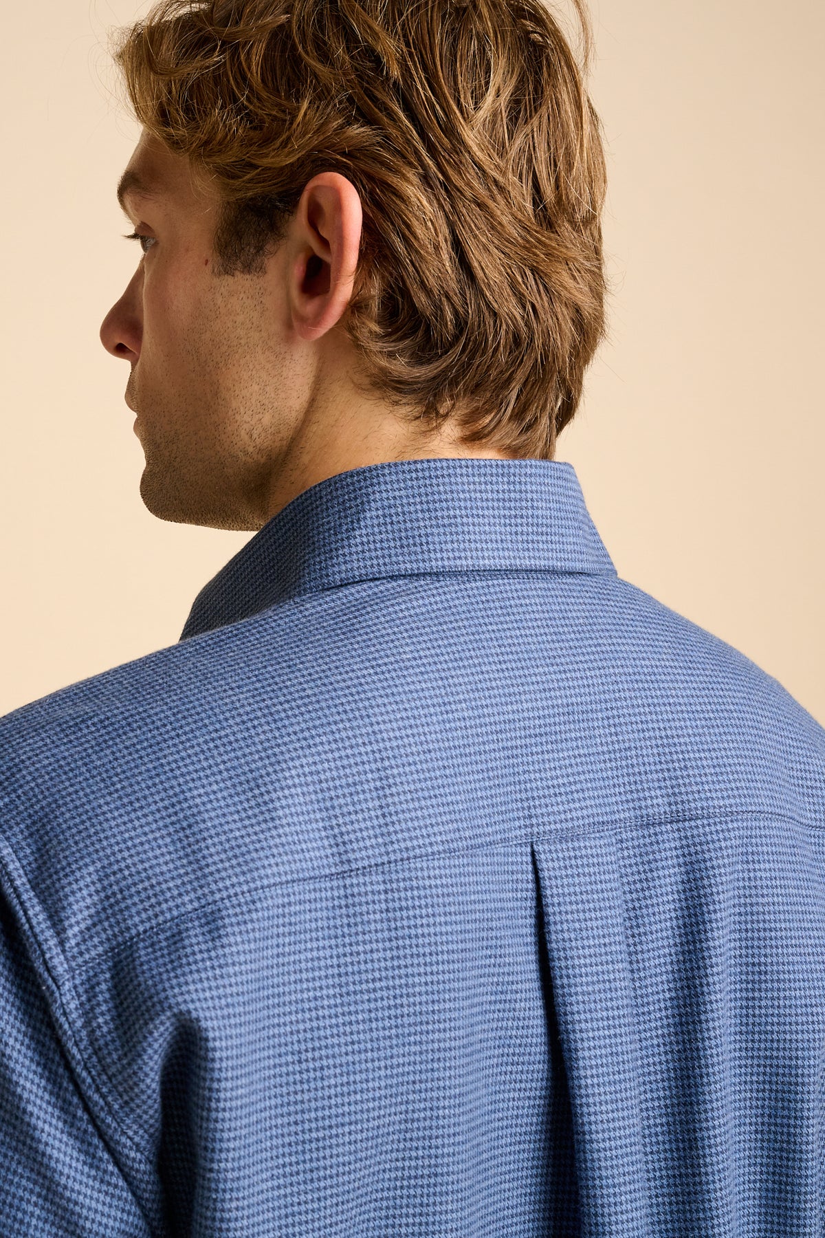 Man wearing blue shirt against beige background.