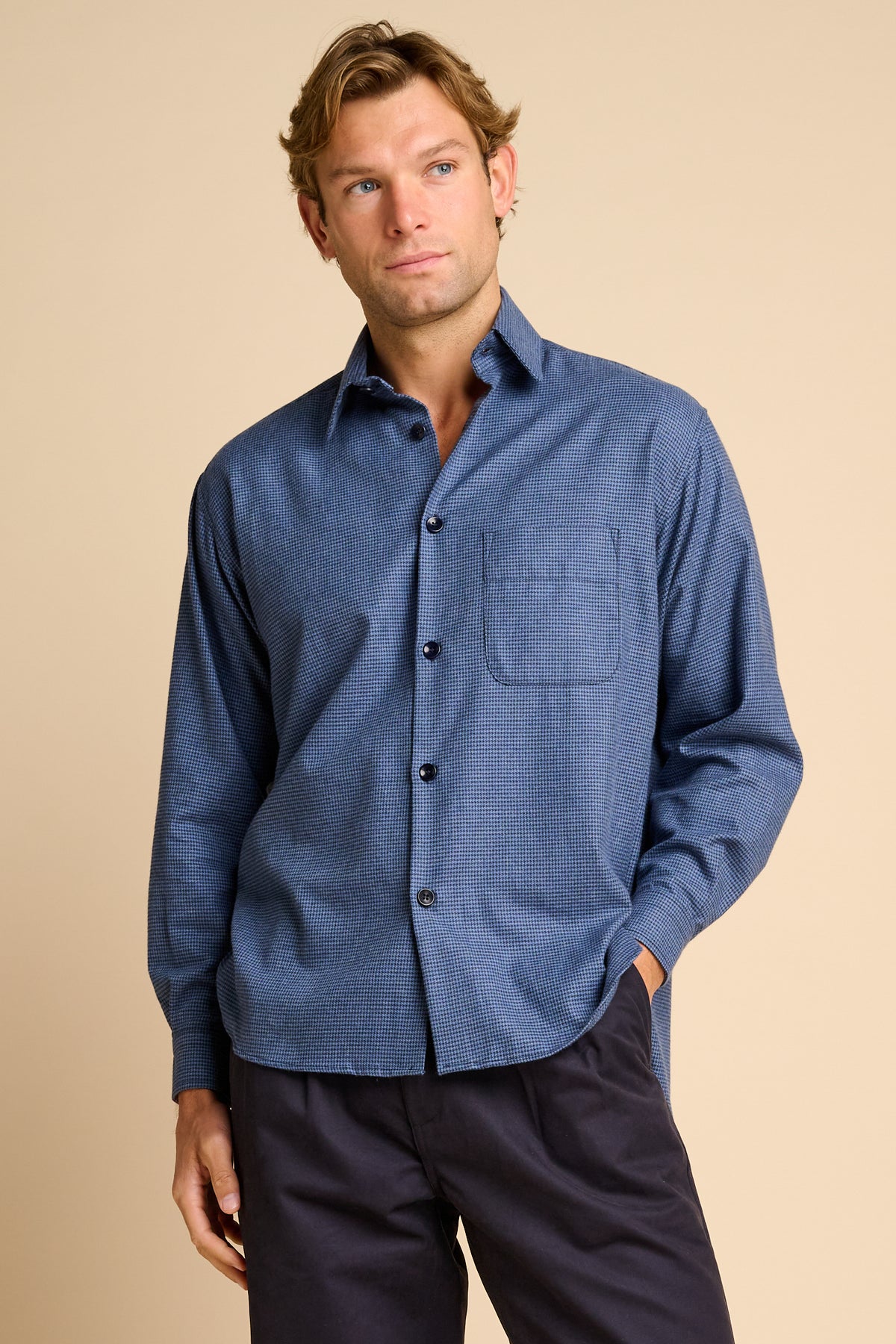 Man wearing blue shirt against beige background.