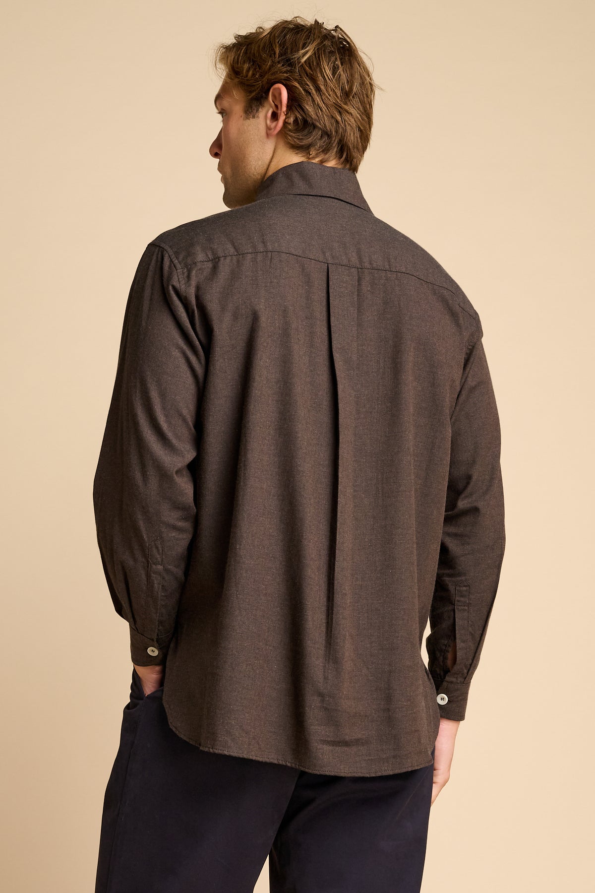Man wearing brown shirt against beige background.