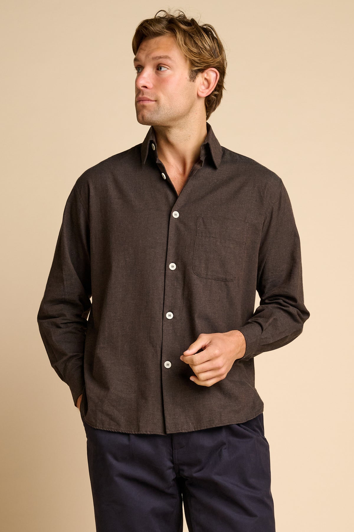 Man wearing brown shirt against beige background.
