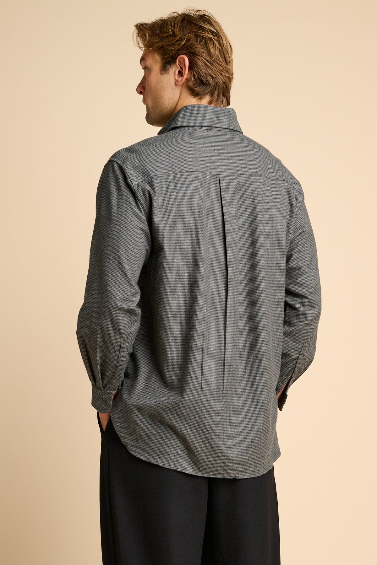 Man wearing grey shirt against beige background.