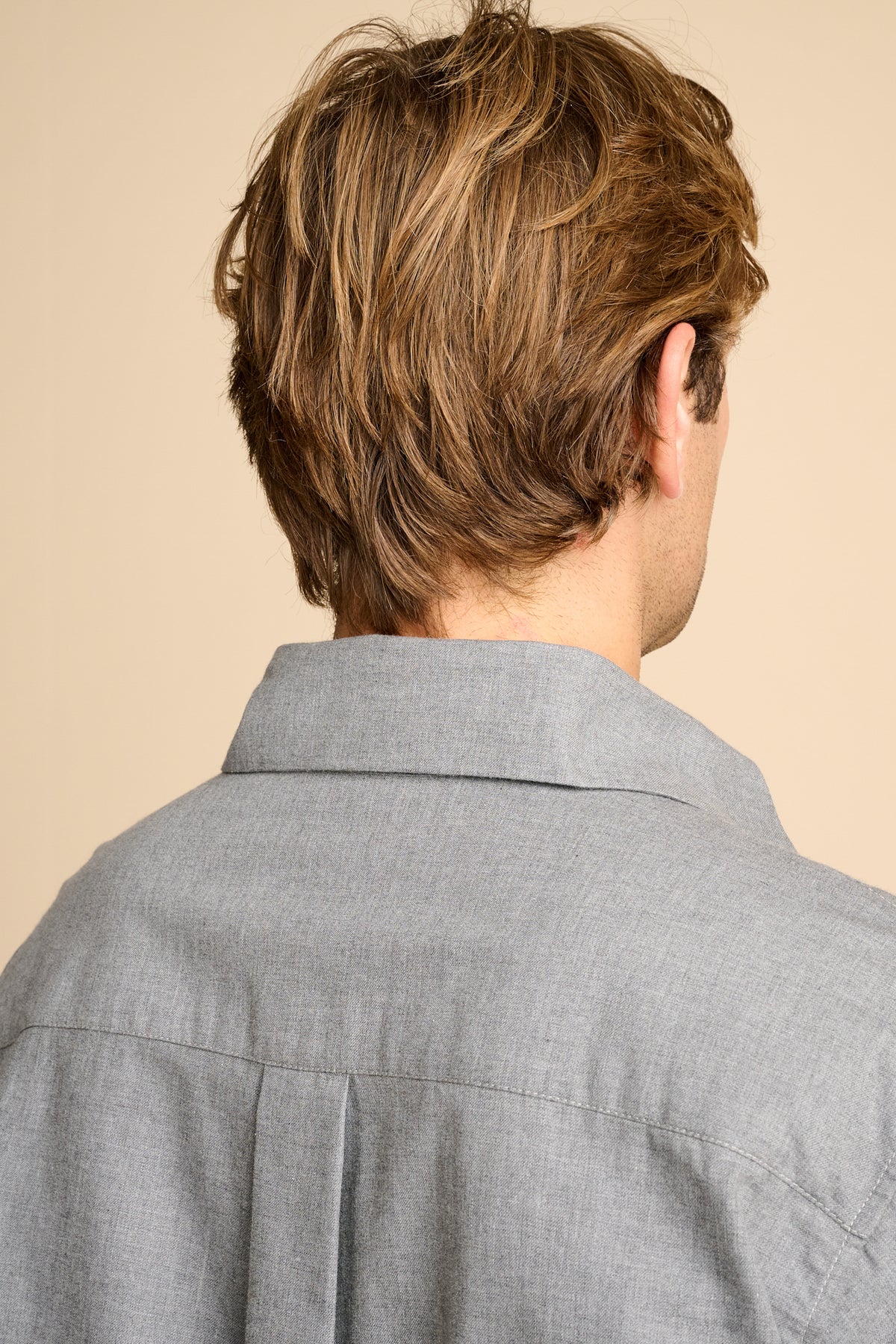 Man wearing grey shirt against beige background.