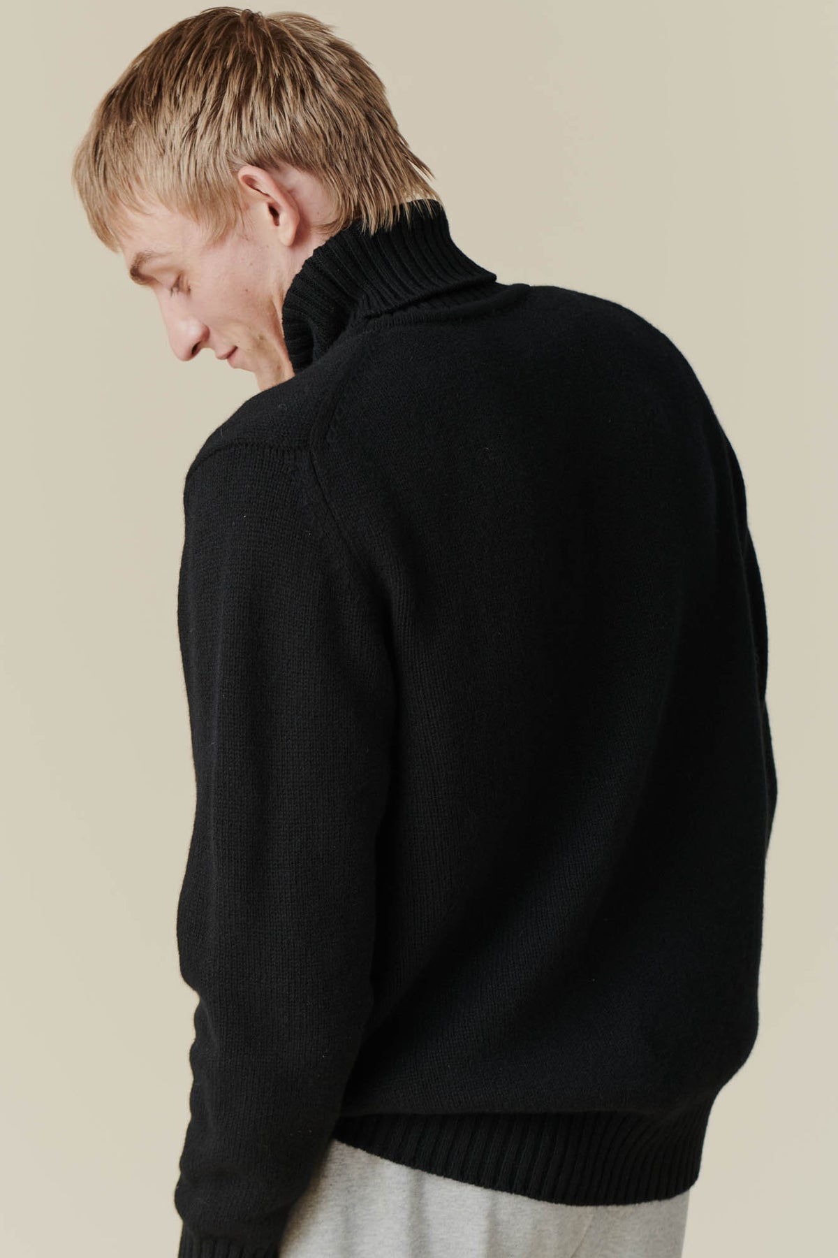 Back of white male wearing lambswool roll neck in black.