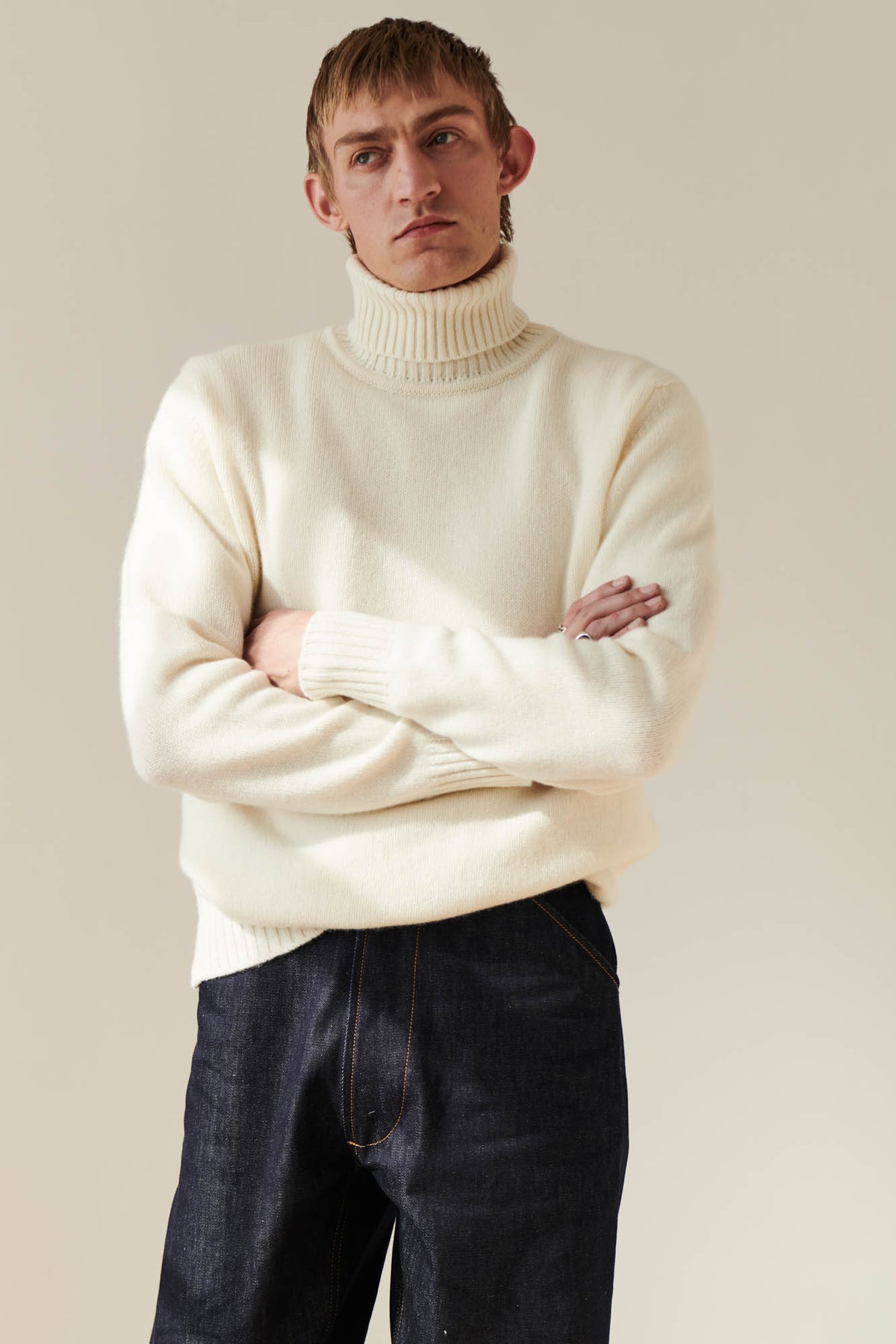 Thigh up shot of male wearing lambswool roll neck in ecru