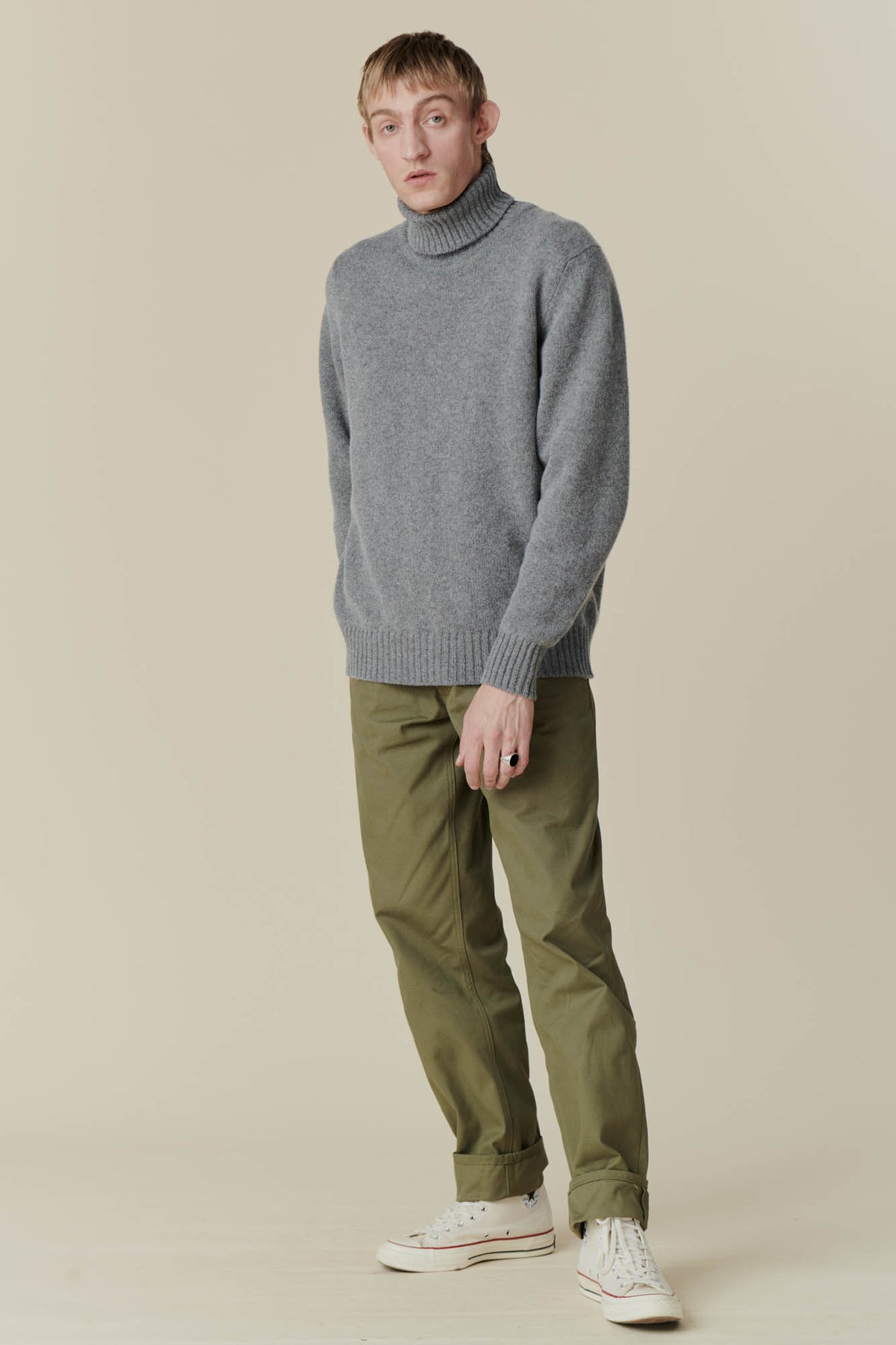Full body shot of male wearing grey roll neck jumper and olive cameraman pant