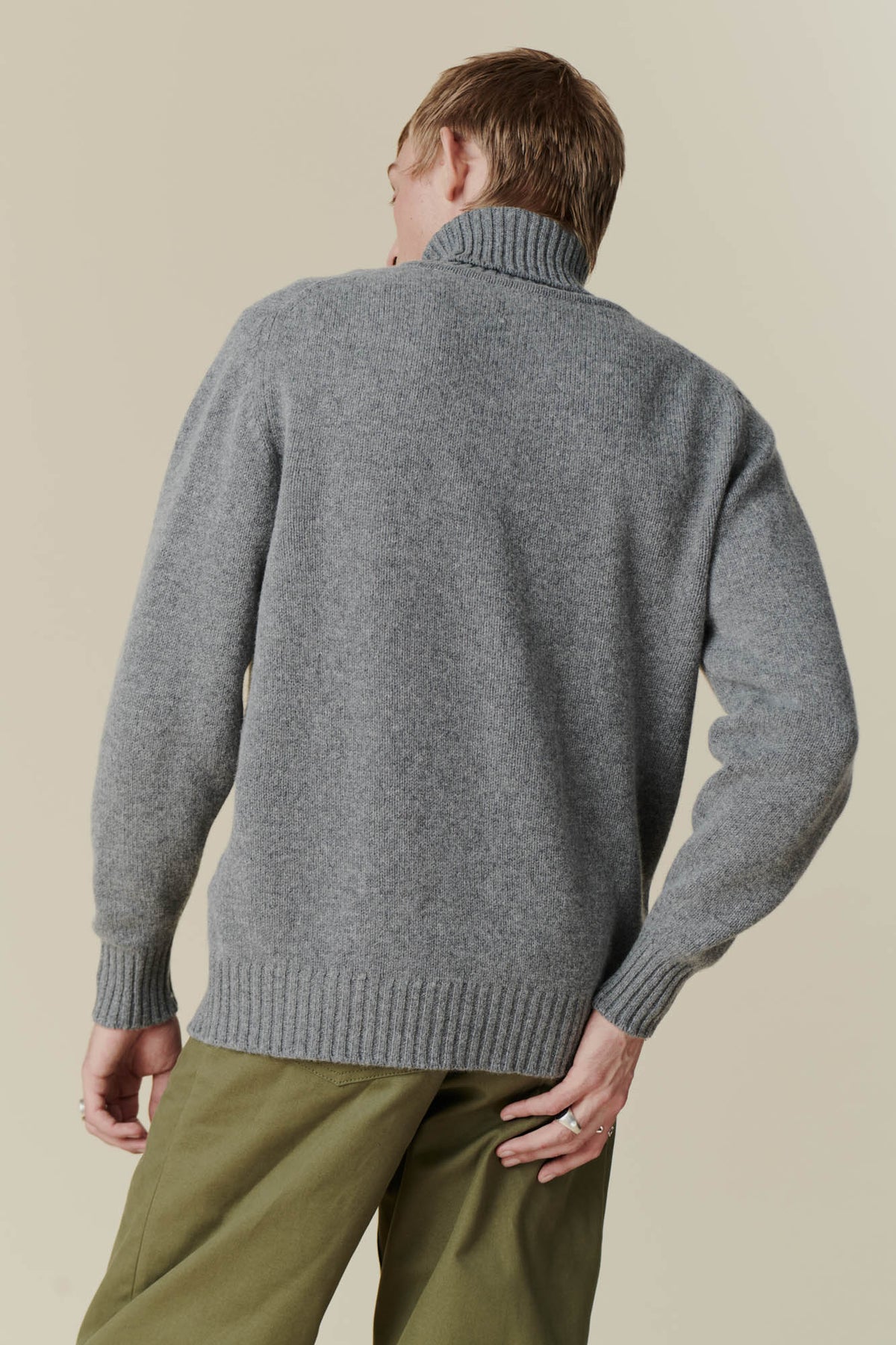 Back shot of male wearing grey roll neck jumper and olive cameraman pant