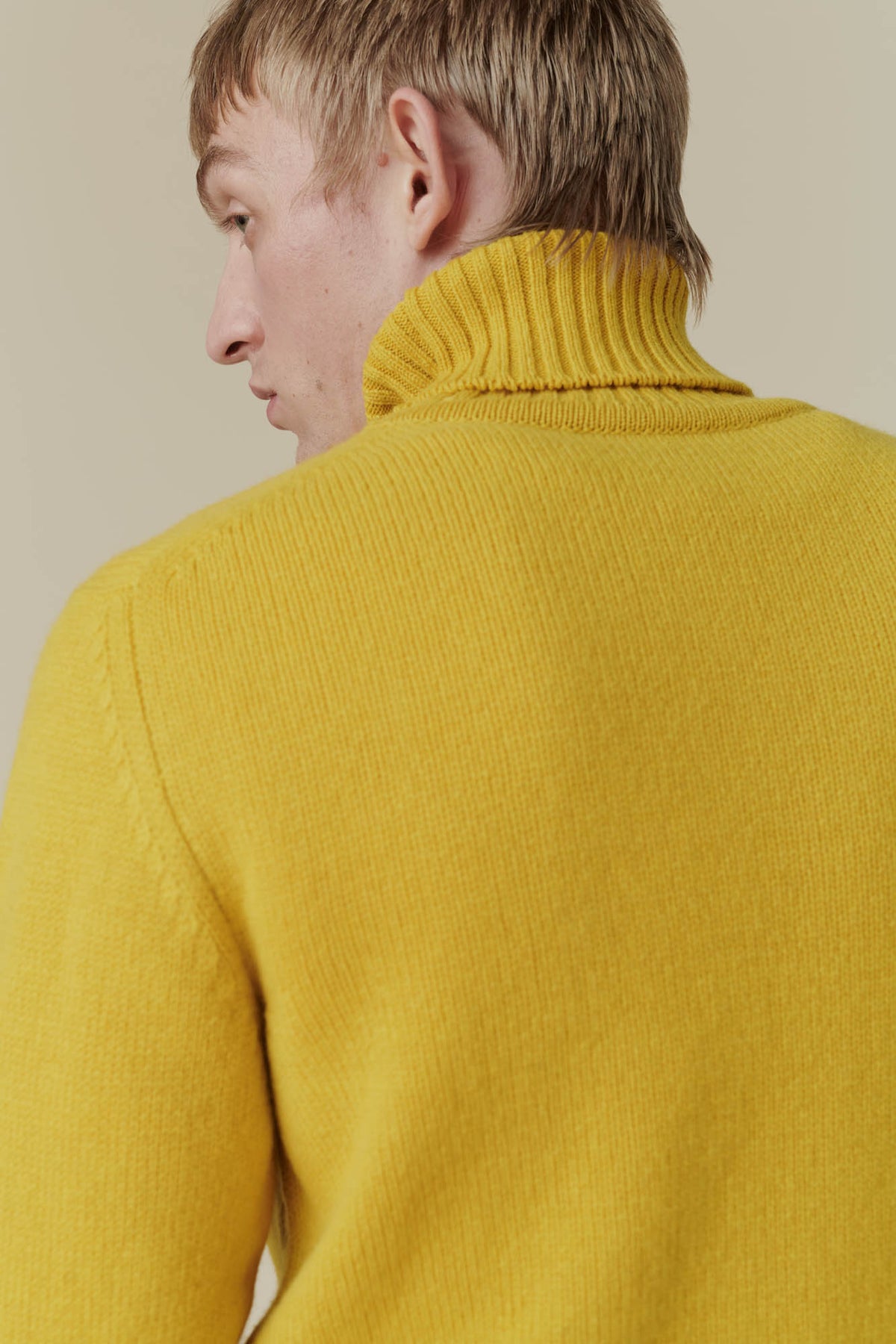 Waist up shot of blonde male wearing mustard lambswool roll neck 