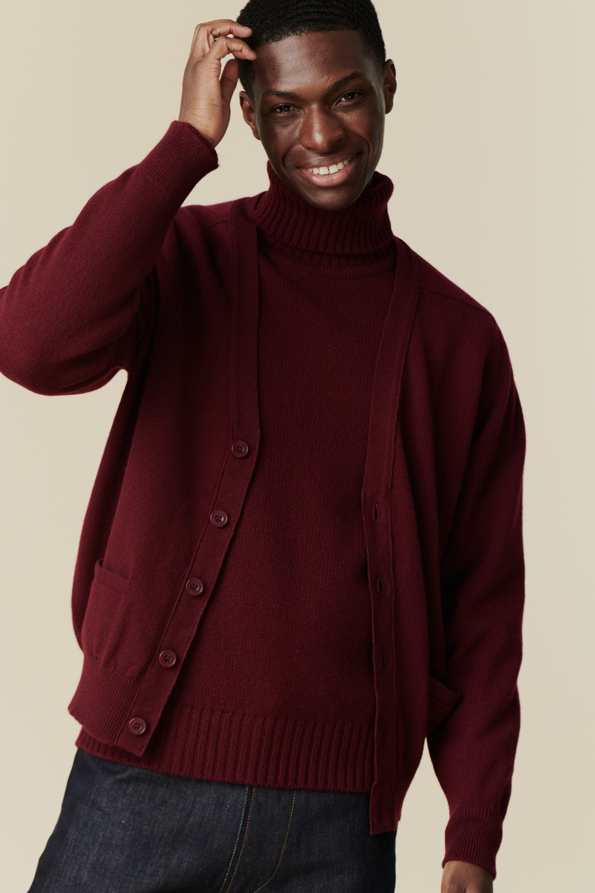 Male wearing lambswool v neck cardigan in burgundy over burgundy roll neck