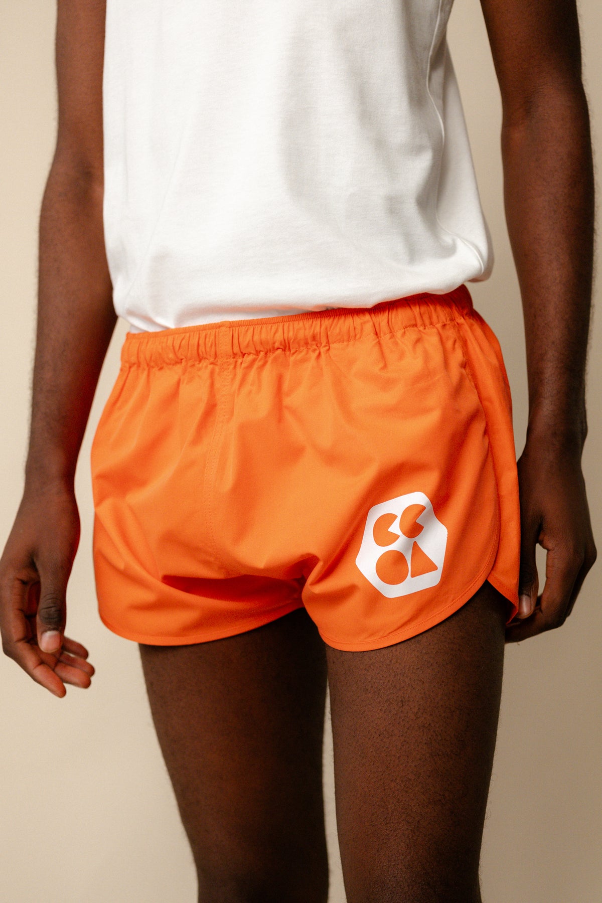 Image showing black male from shoulder to knee wearing men's lightweight running short plastic free in flame red with white CCOA logo