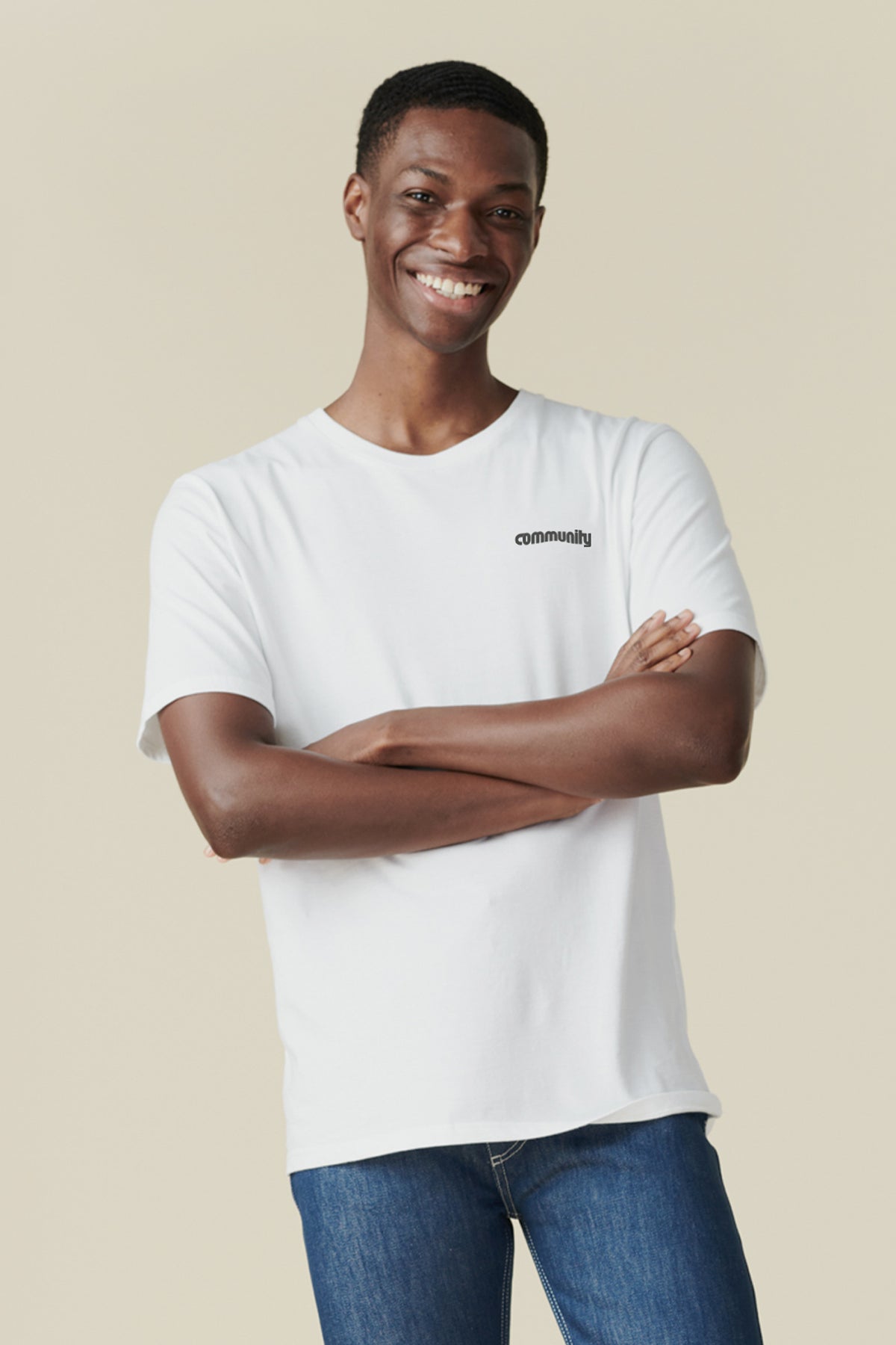 Thigh up image of smiley, black male with arms folded wearing white t shirt with community logo in black on chest