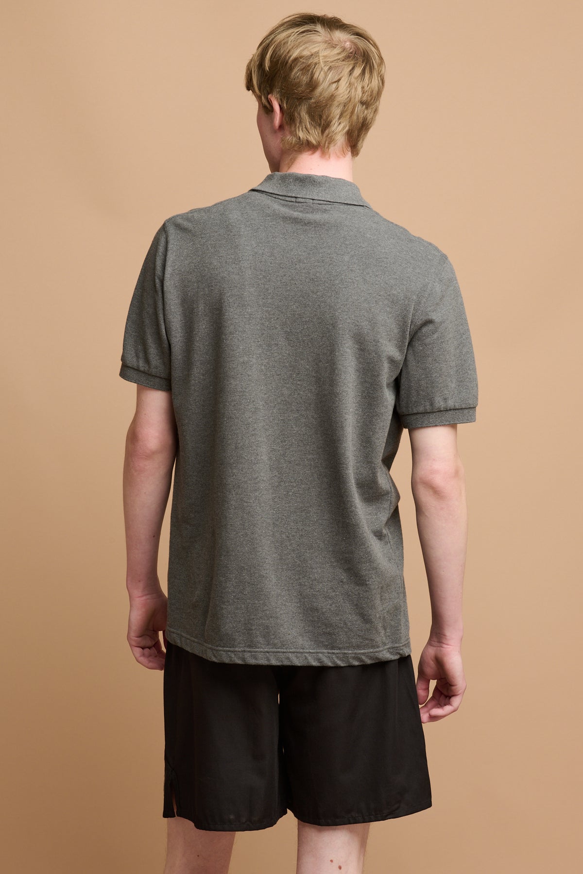 the back of male wearing long lightweight running shorts in black paired with short sleeve polo shirt in grey