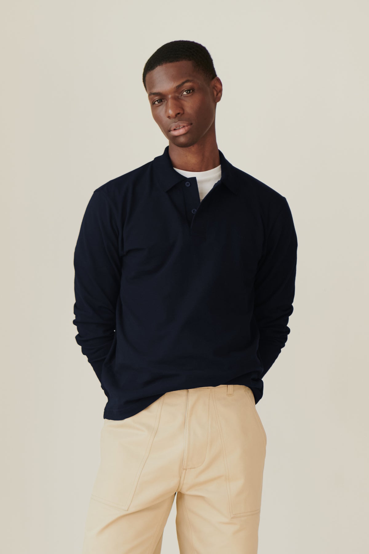 black male wearing a navy long sleeve community clothing polo shirt with putty coloured combat pant