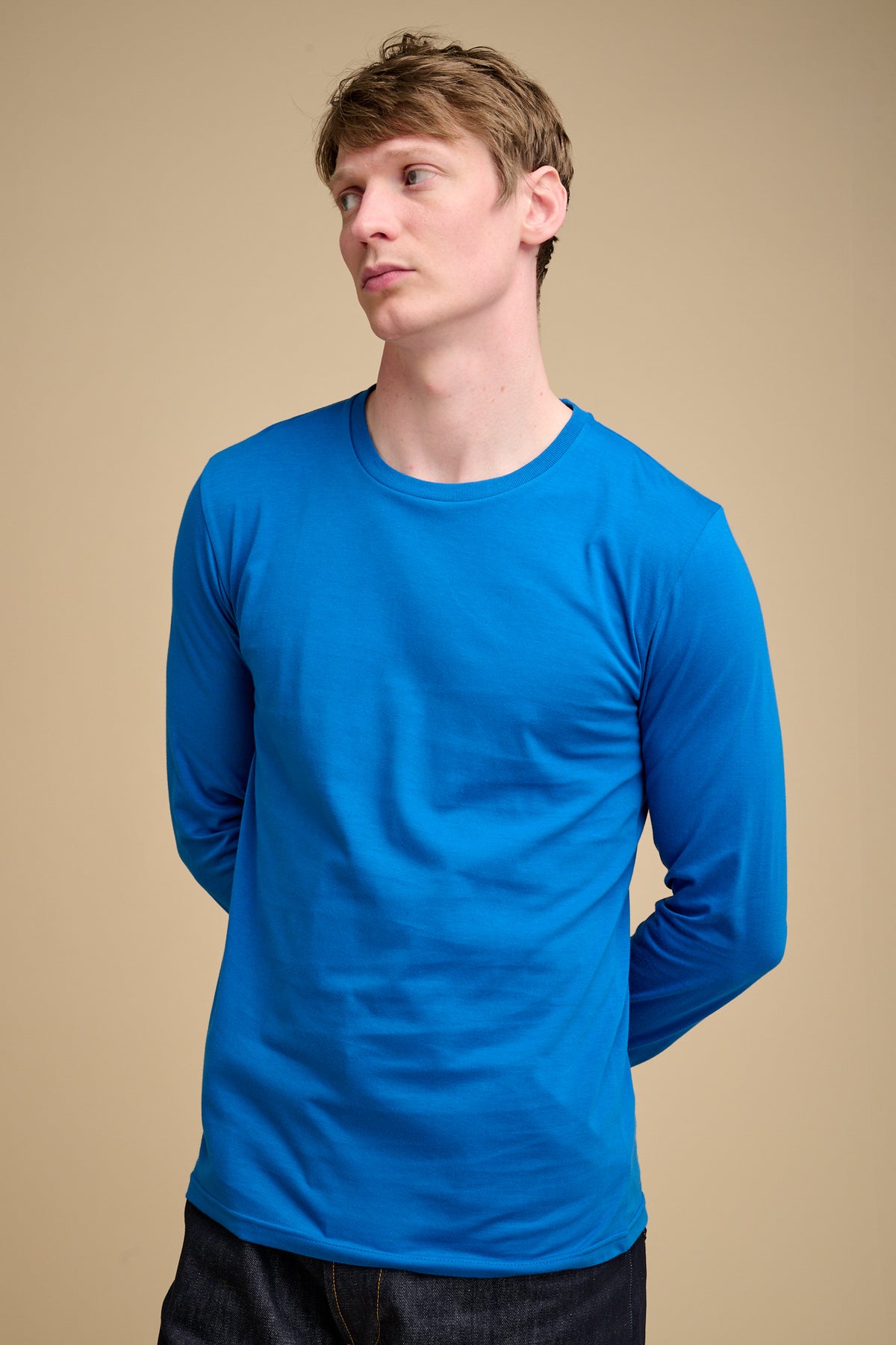 Man wearing a cobalt blue long-sleeve t-shirt against a beige background.