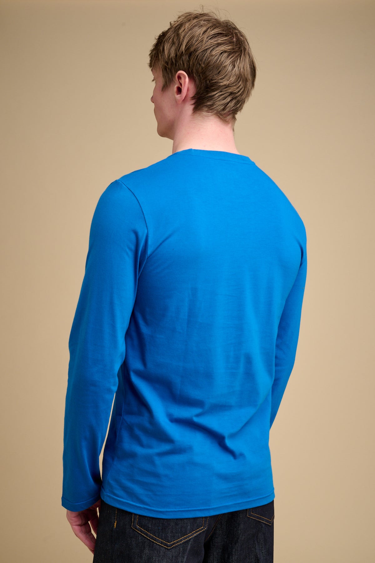 The back of man wearing a blue long-sleeve t-shirt against a beige background.