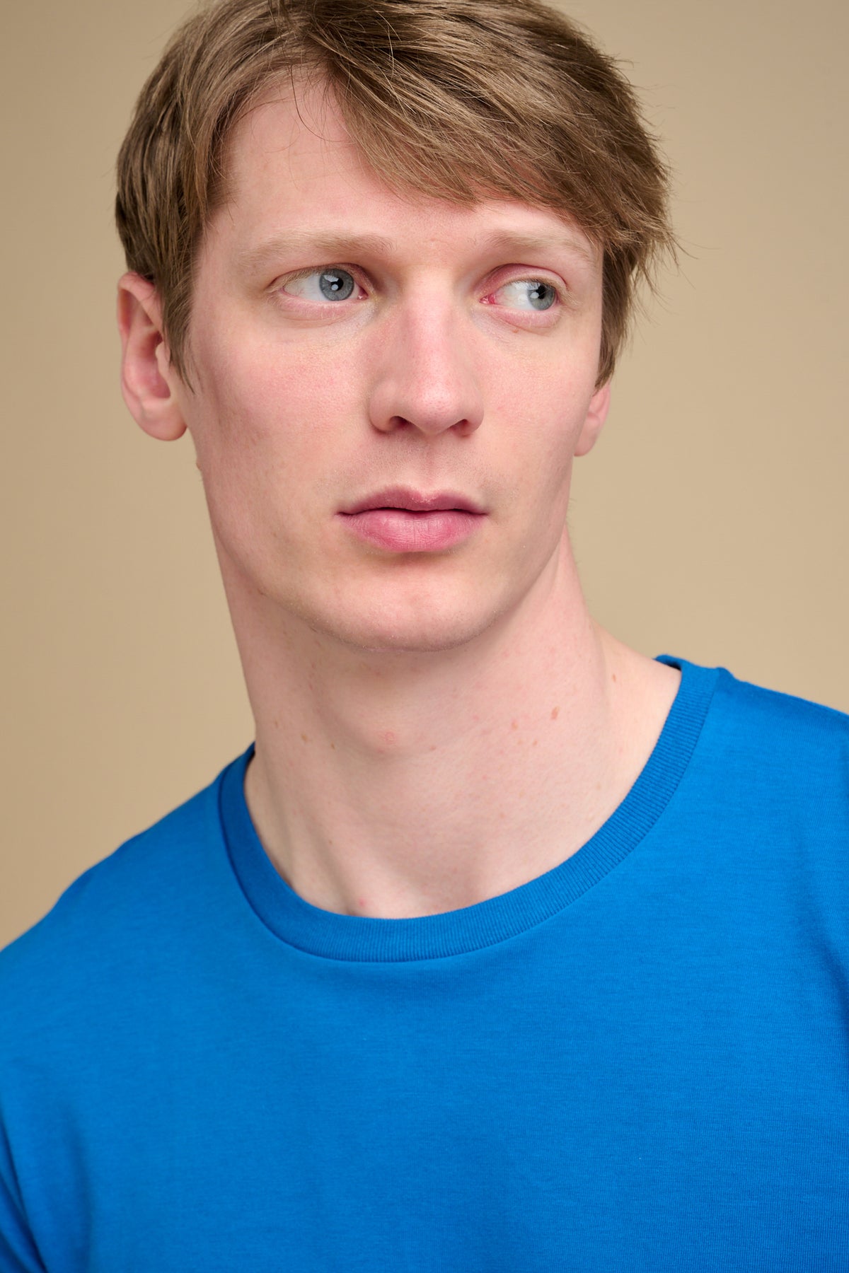 Man wearing a blue long-sleeve t-shirt against a beige background.