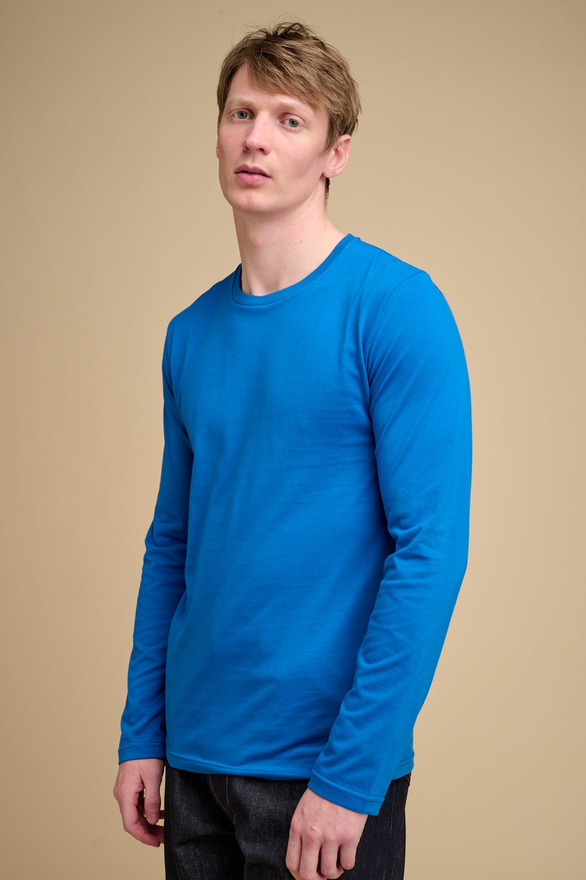Man wearing a cobalt blue long-sleeve t-shirt against a beige background.
