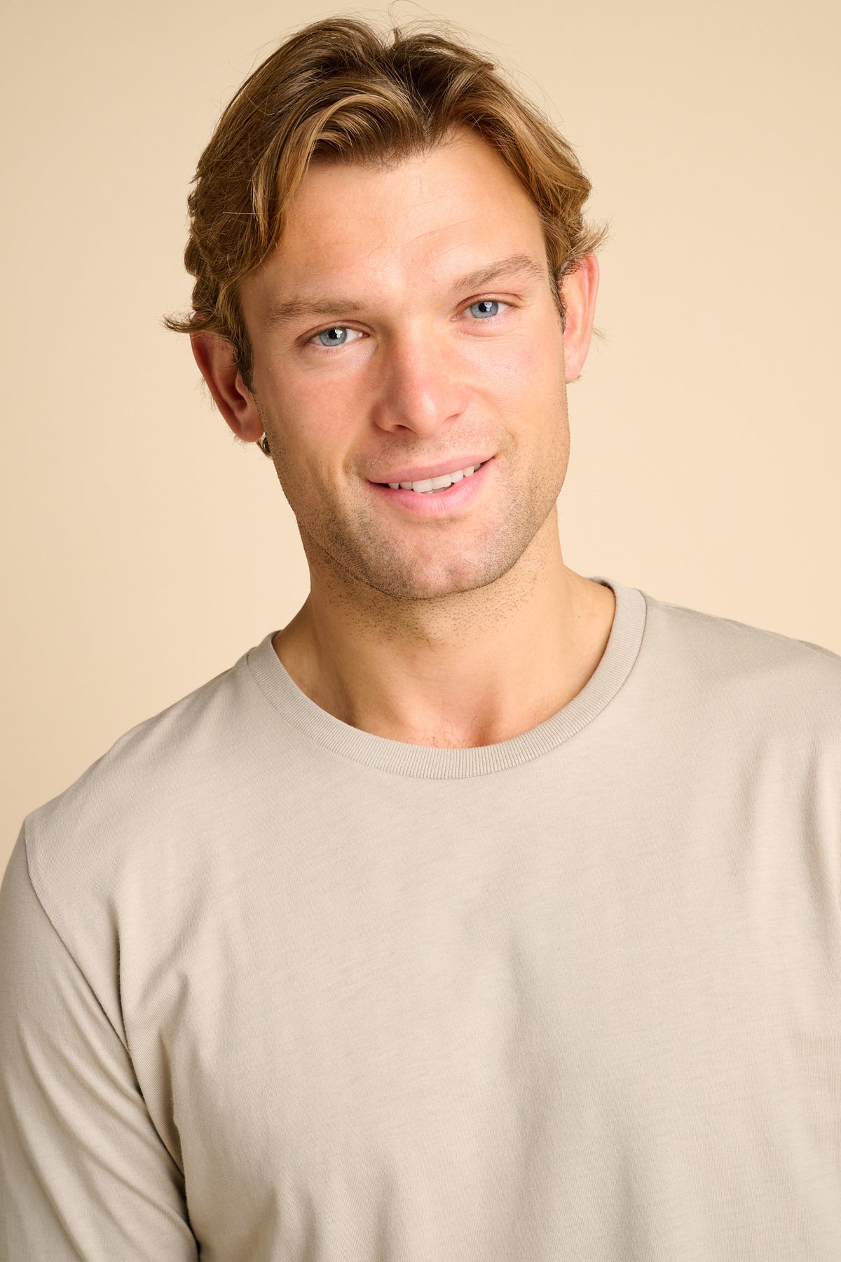 Man wearing stone shirt against beige background. 