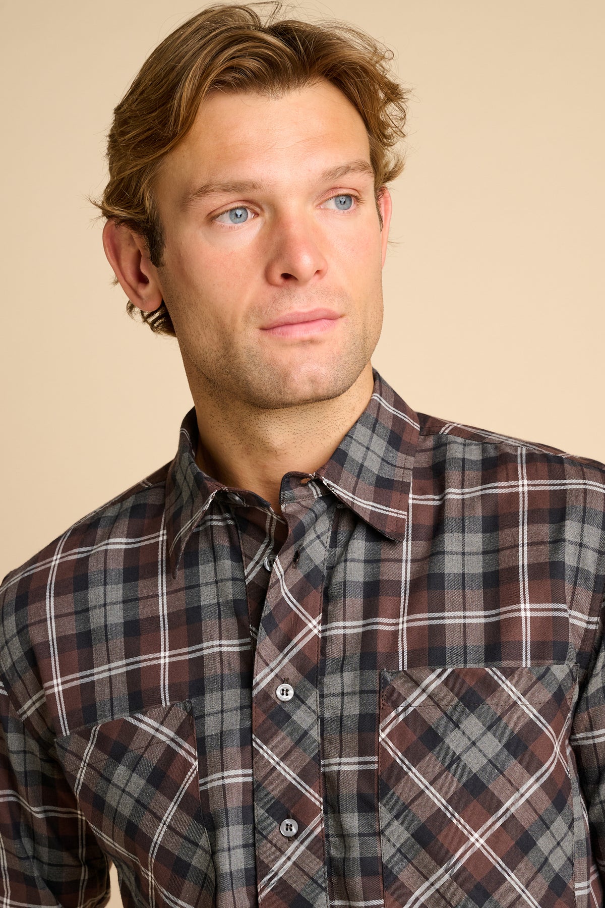 Man wearing check shirt against beieg background.