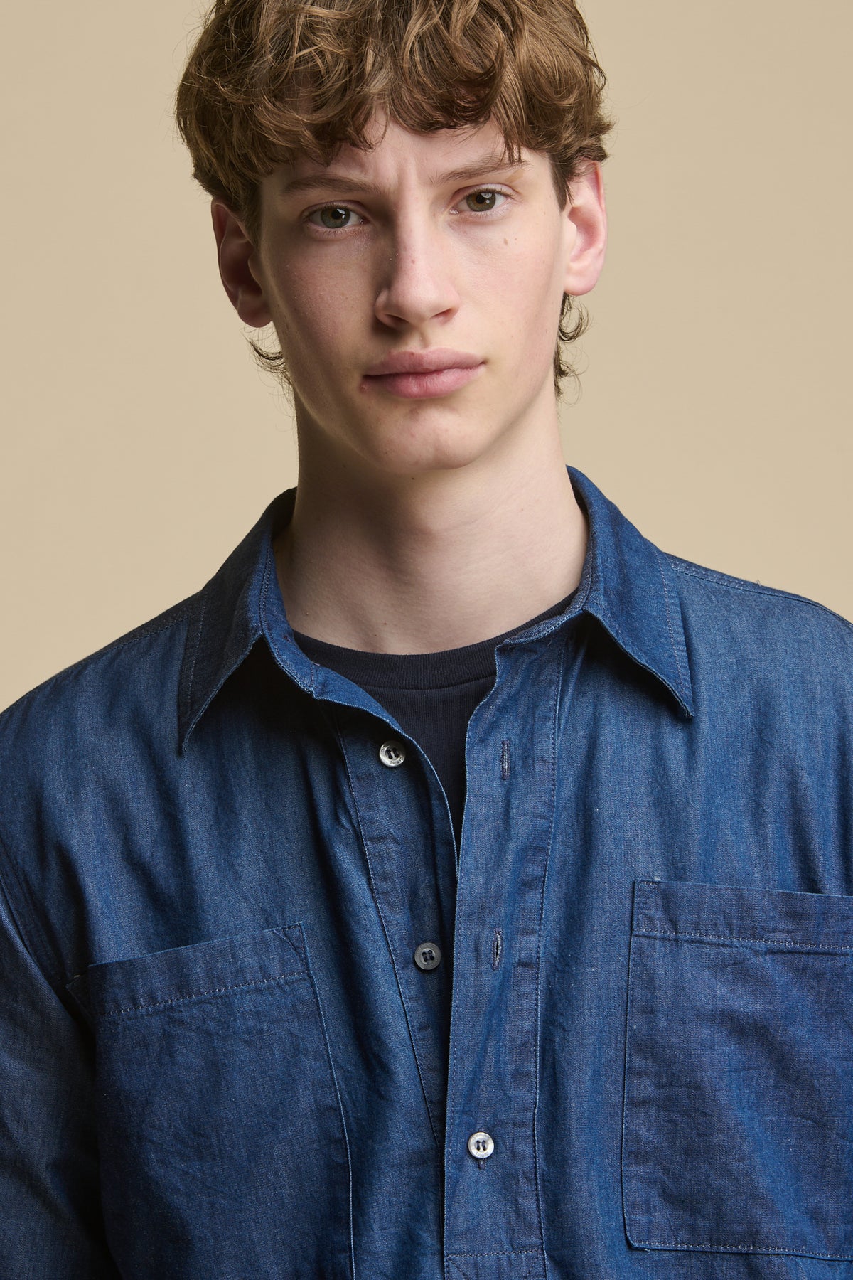Portrait of male showing the half placket detail and front pockets of men's half placket lightweight denim shirt worn over navy short sleeve t shirt