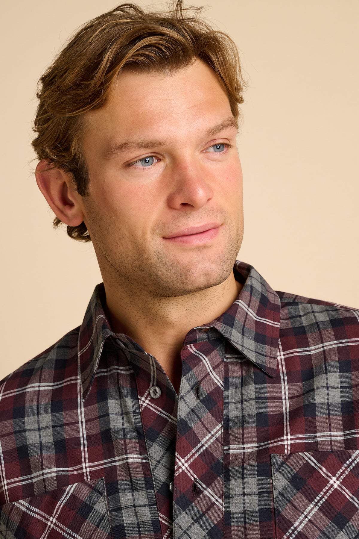 Man wearing red check shirt against beige background.