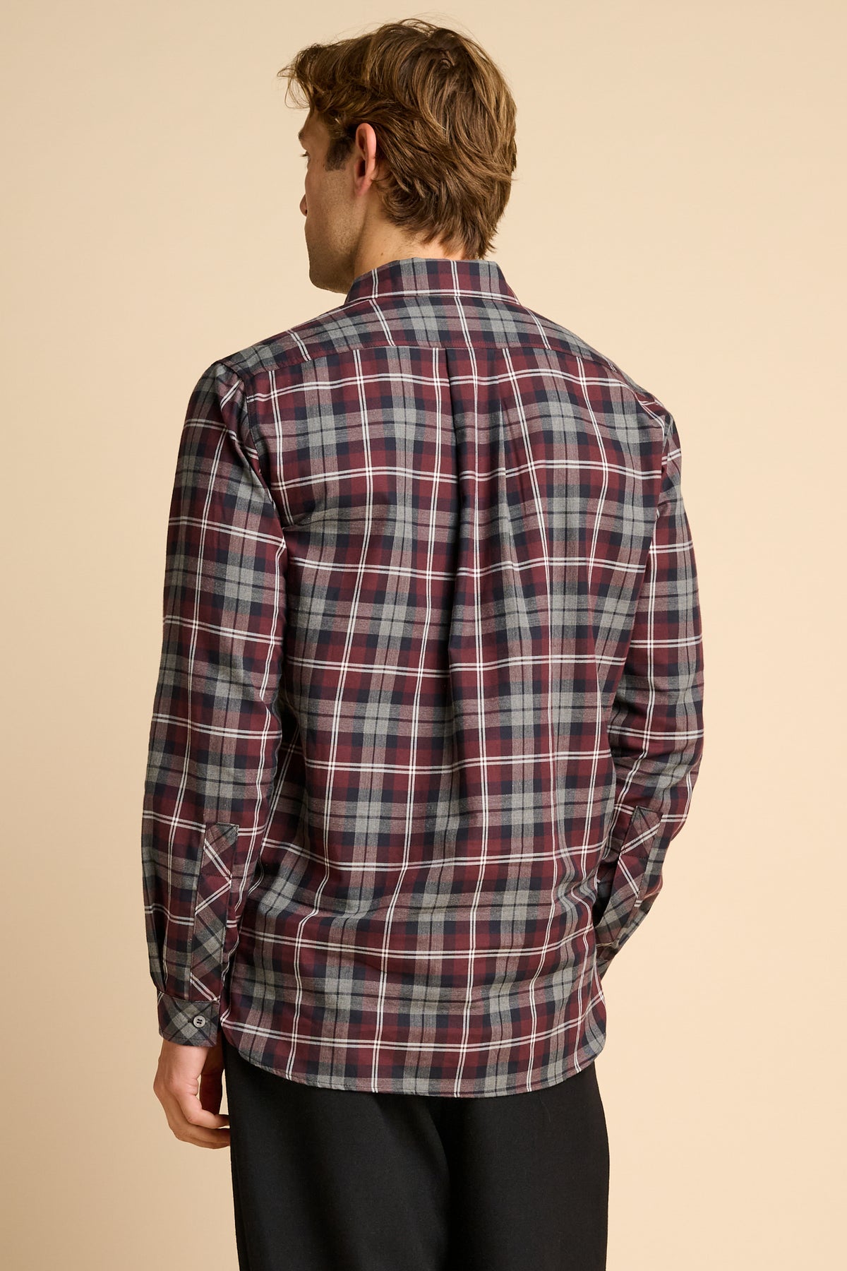 Man wearing red check shirt against beige background.
