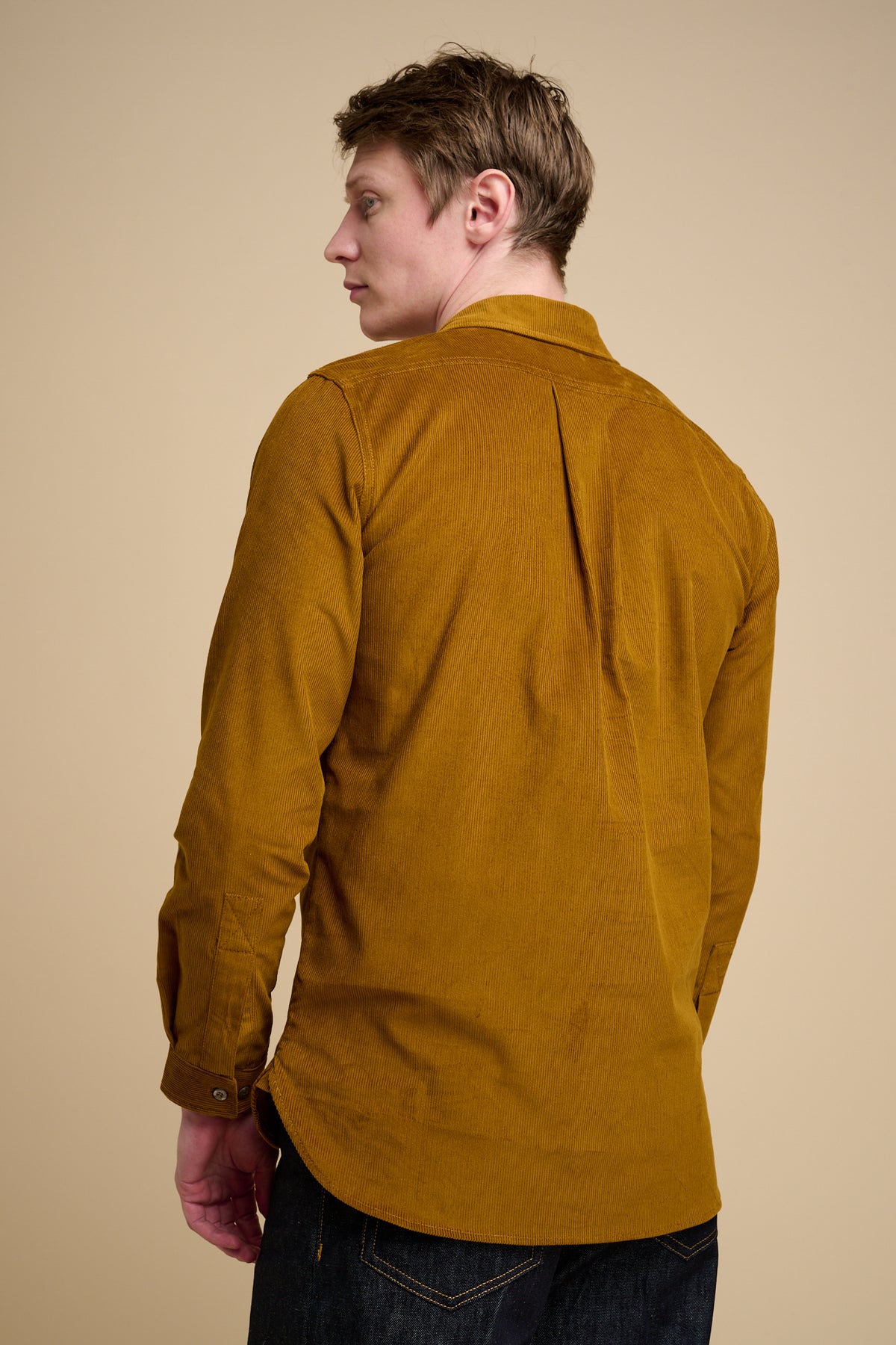 The back of man wearing half placket needle cord shirt in mustard.