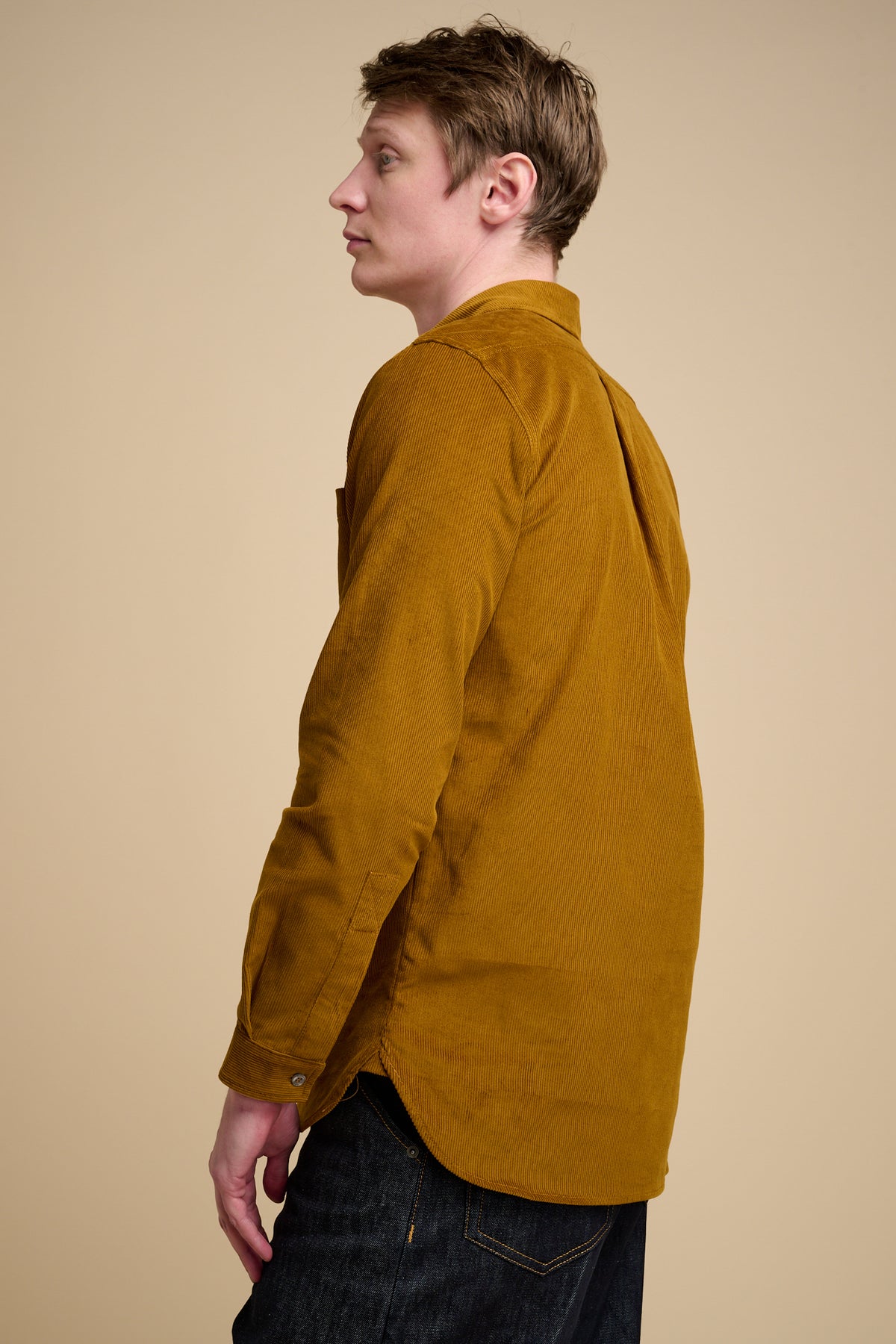The side of male wearing half placket needle cord shirt in mustard.