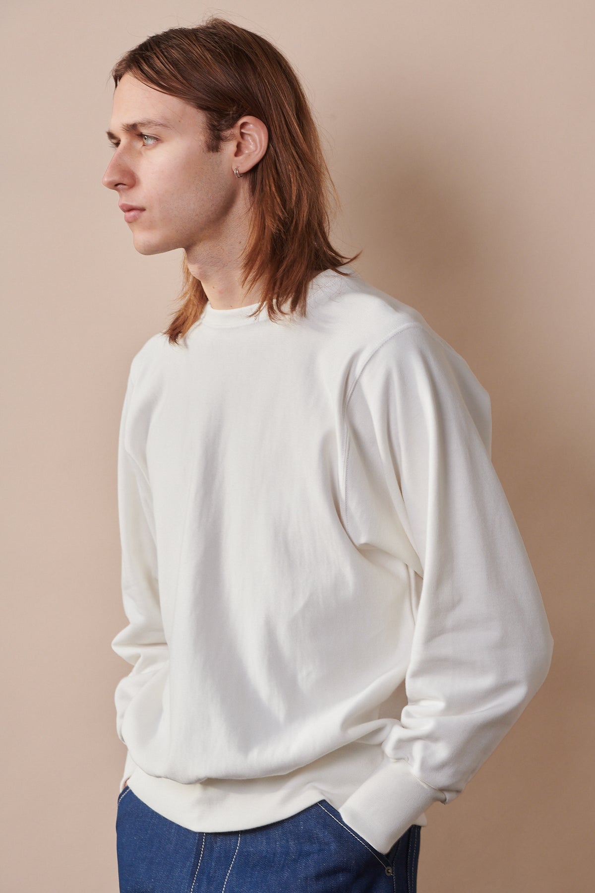 Hip up of male wearing crew neck 80s sweatshirt in bone with hands in jean pockets 
