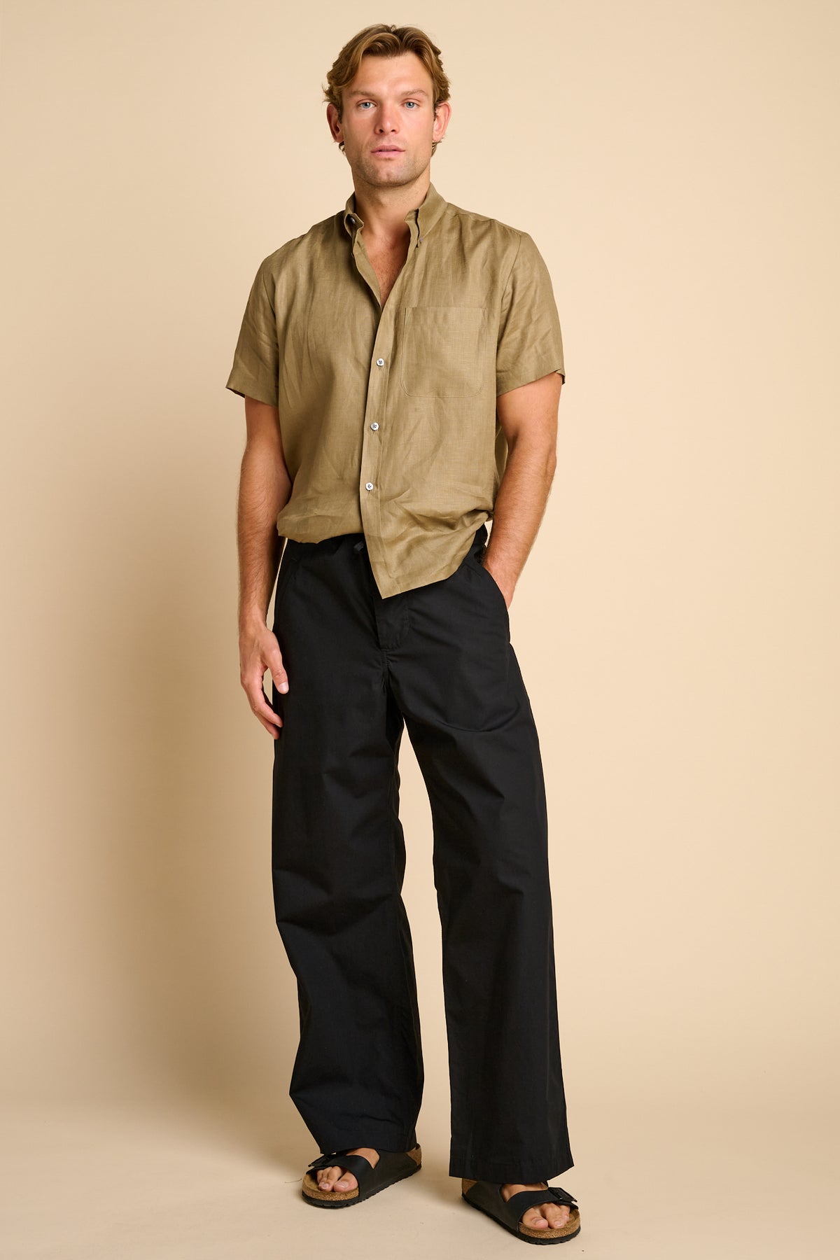 Man wearing black trousers against beige background. 