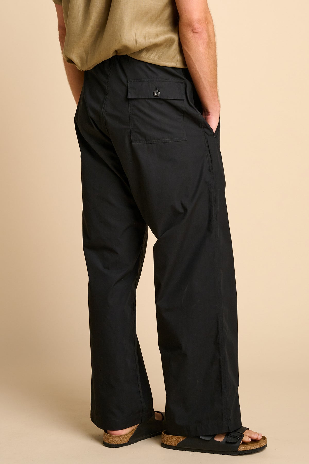 Man wearing black trousers against beige background. 