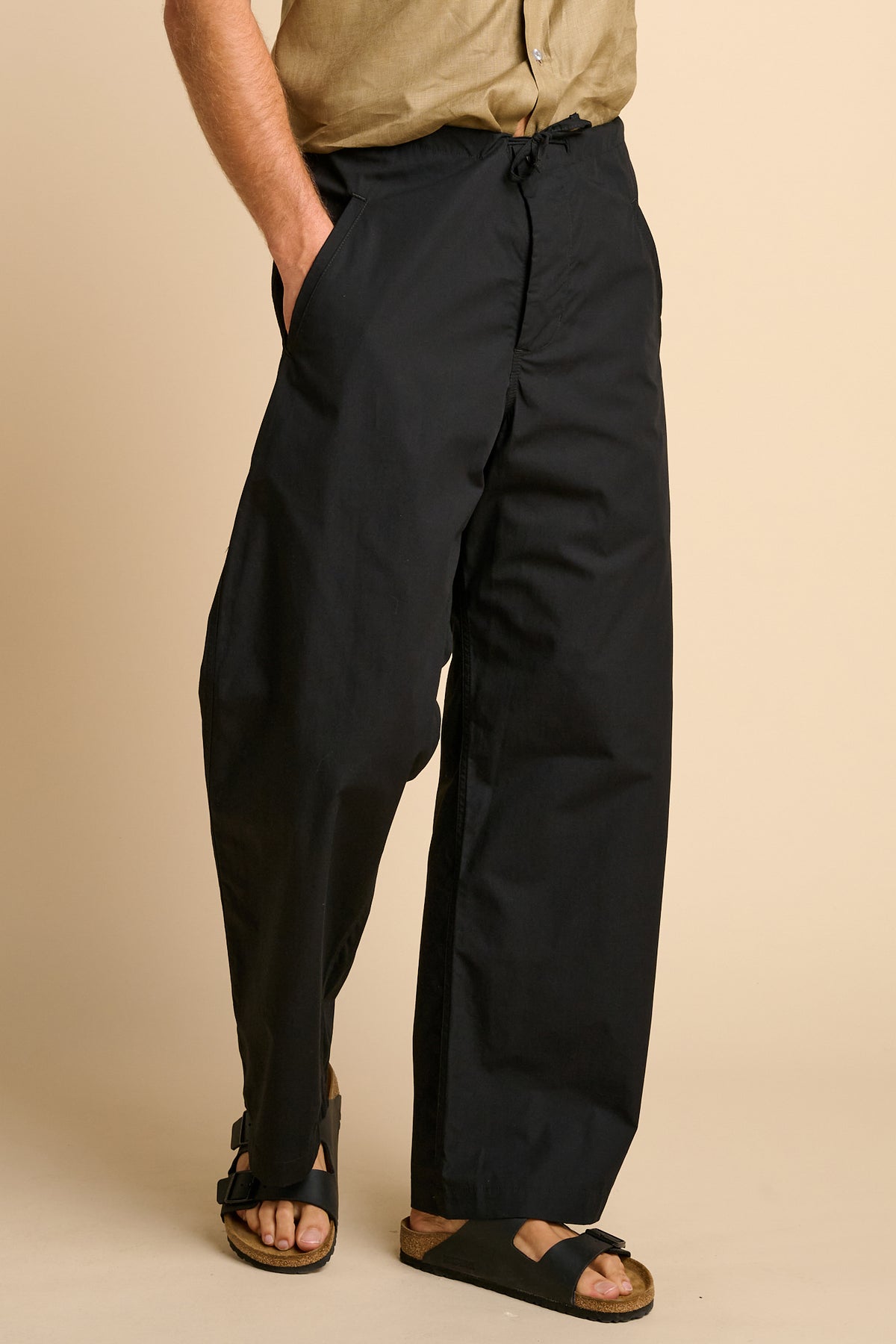 Man wearing black trousers against beige background. 