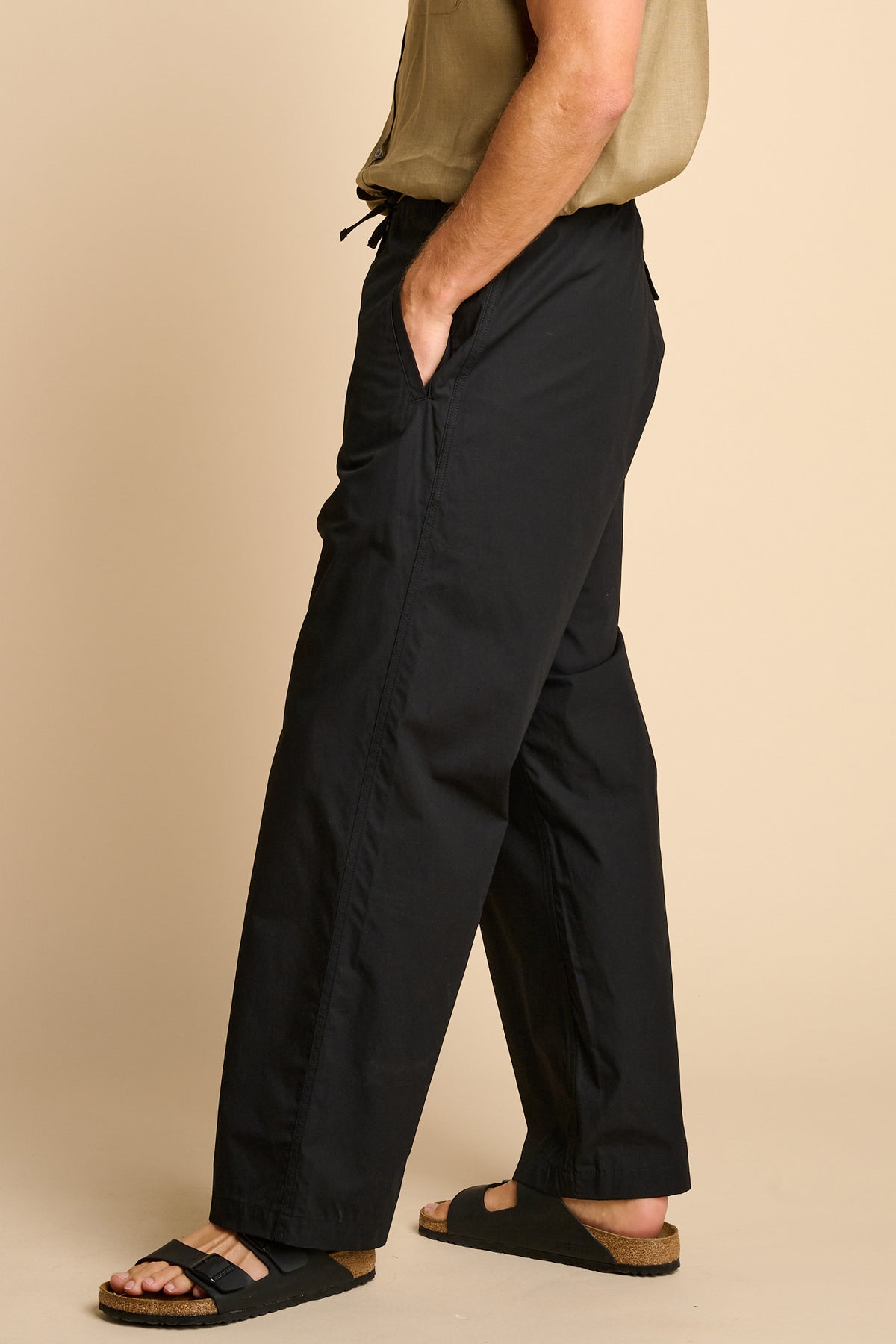 Man wearing black trousers against beige background. 