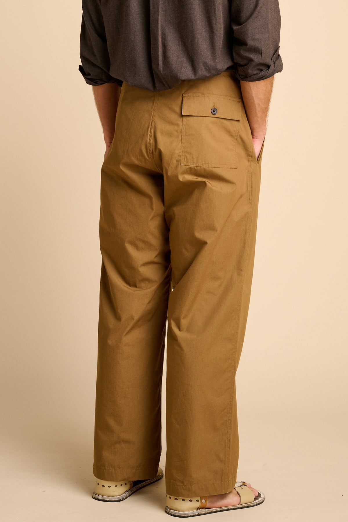 Man wearing tan trousers against beige background.