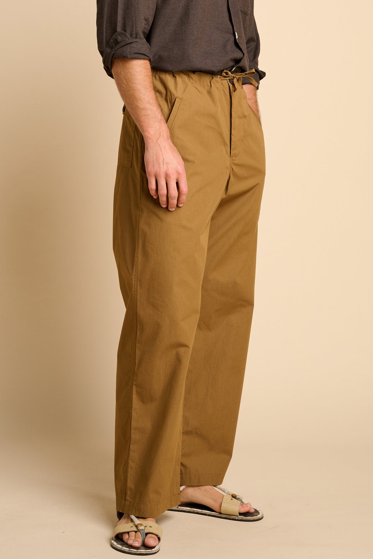 Man wearing tan trousers against beige background.