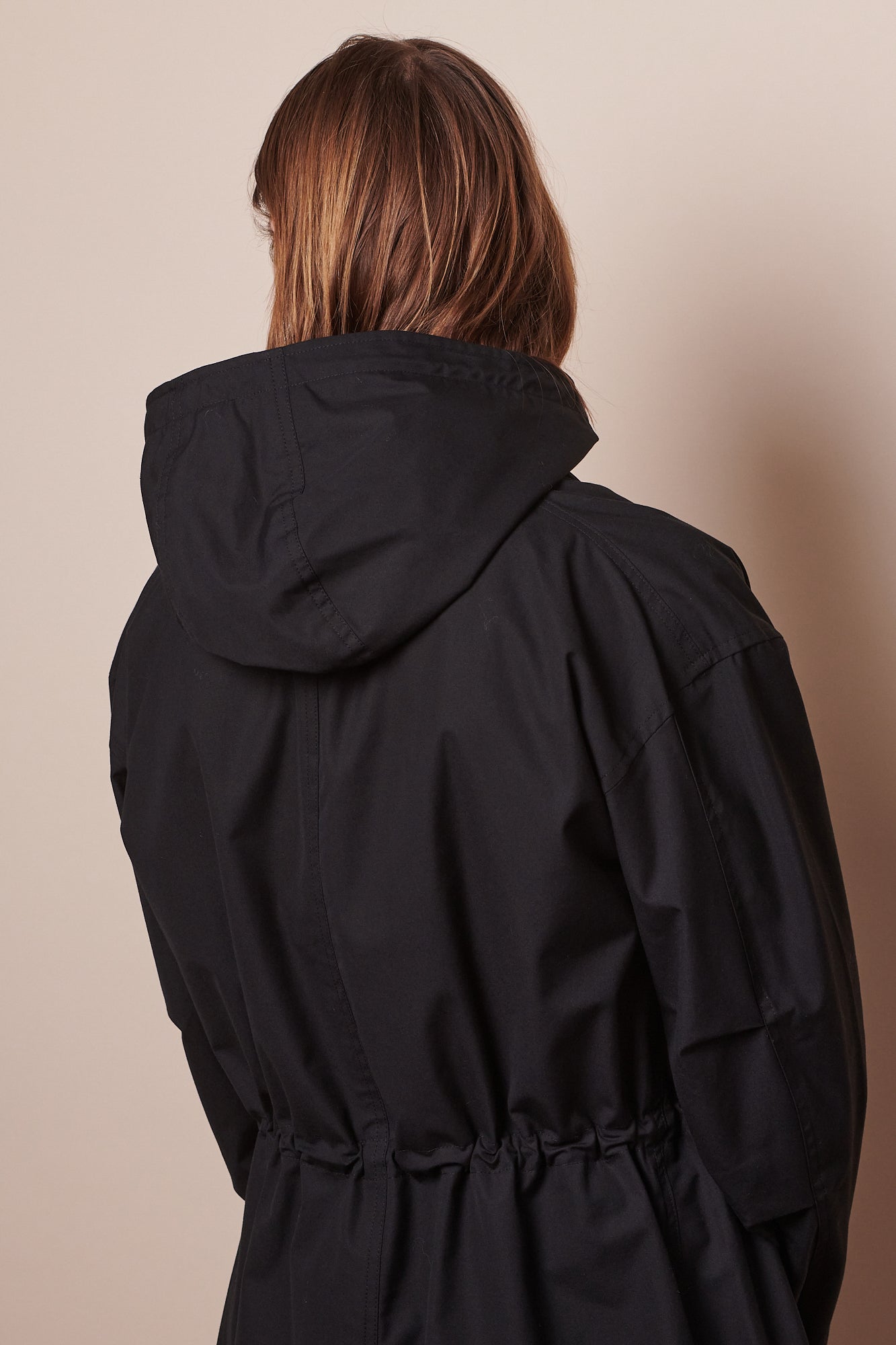 Full body image of male wearing black parka unzipped holding hands behind back.