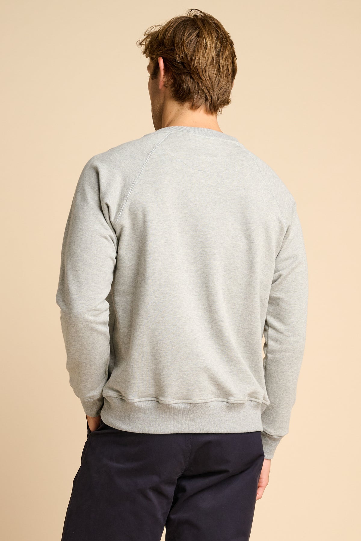 Man wearing a grey sweatshirt and dark pants on a beige background.