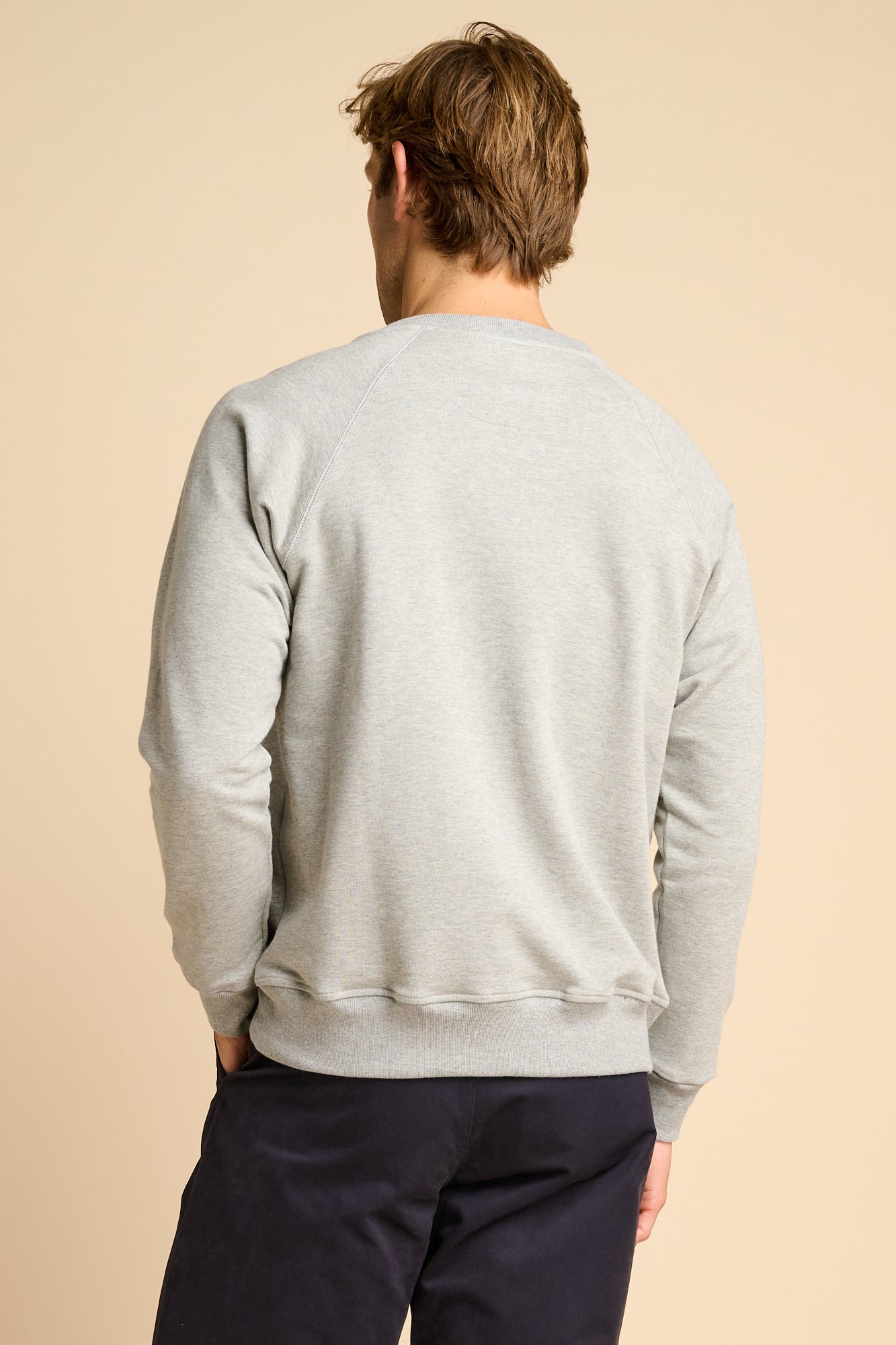 Man wearing a grey sweatshirt and dark pants on a beige background