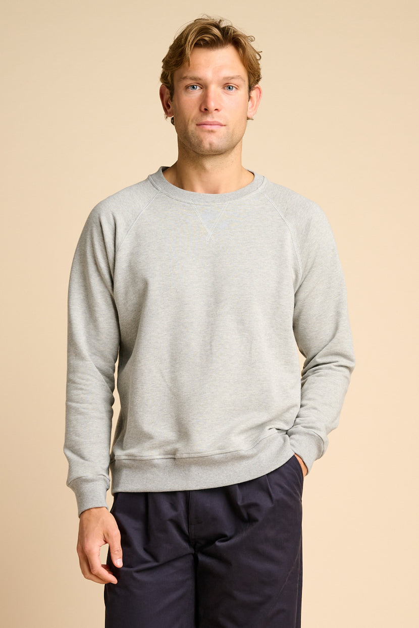 Man wearing a grey sweatshirt and dark pants on a beige background