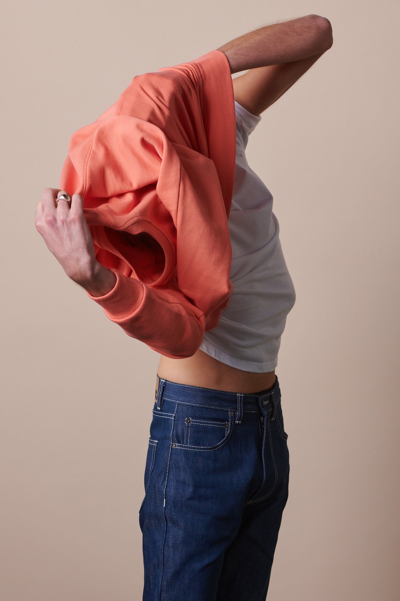 Portrait of male with shoulder length brown hair wearing raglan sweatshirt in peach over crew neck white t shirt.