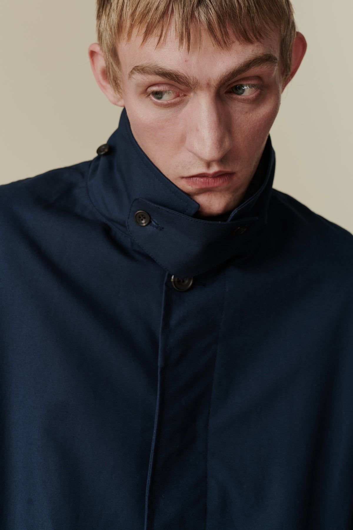 Chest up portrait of white male wearing raincoat in navy. Showing detachable turn up collar detail