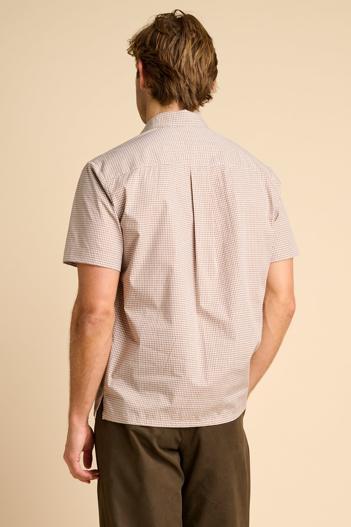 Man wearing a patterned shirt and brown pants on a beige background